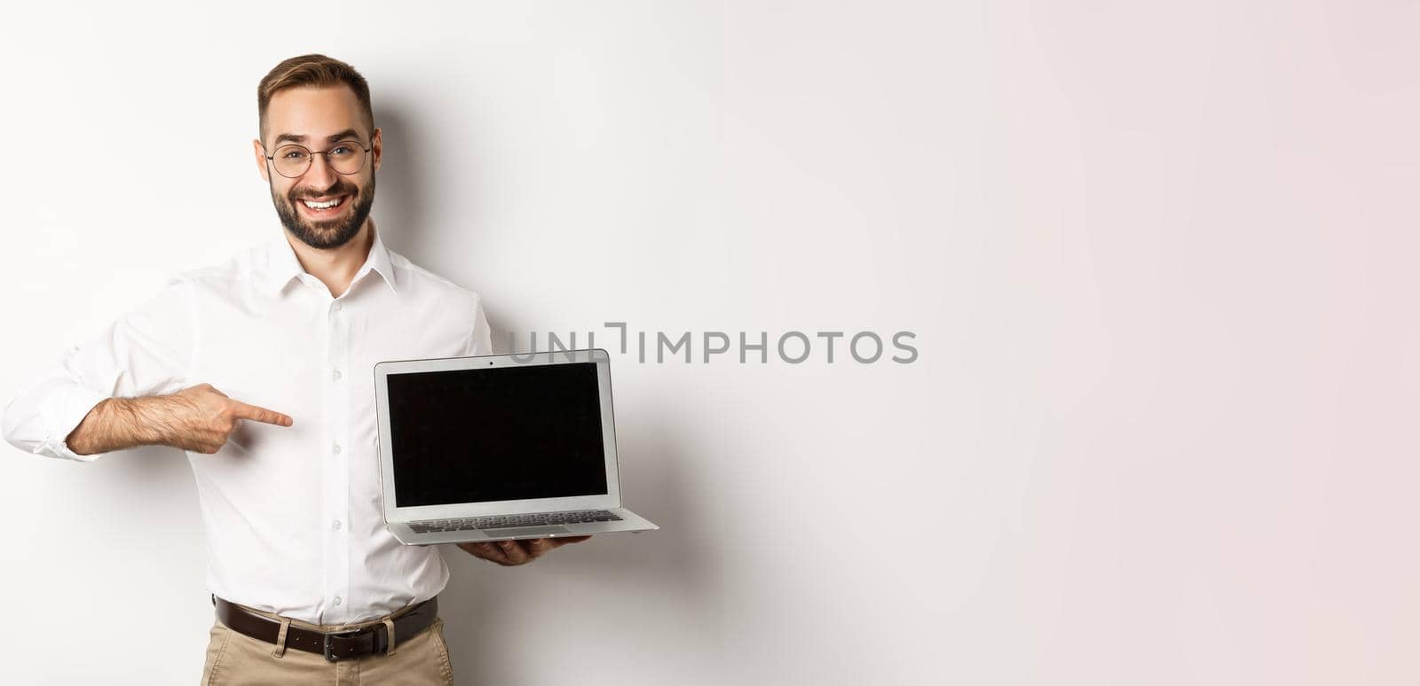 Professional manager showing webpage on laptop screen, pointing at computer, standing over white background.