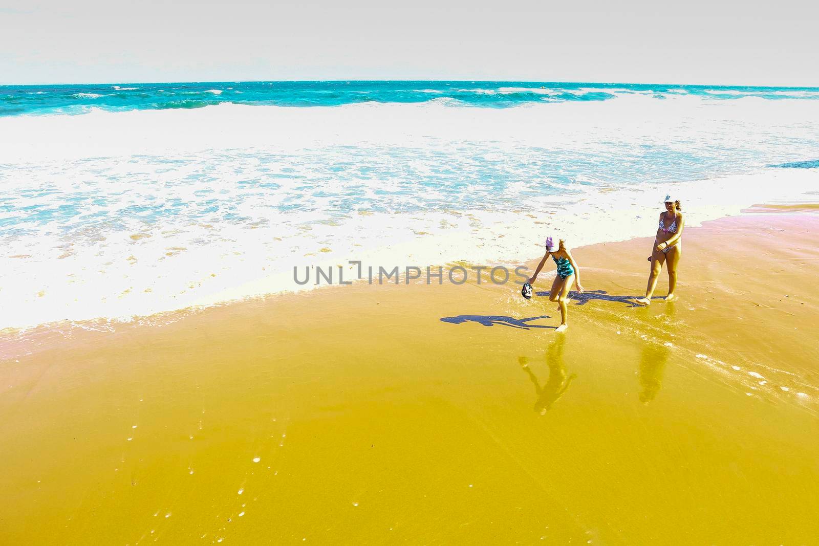 Arenales del Sol, Alicante, Spain- September 18, 2022: Mother and daughter sunbathing and walking by the shore on the beach on a Sunny day of Summer