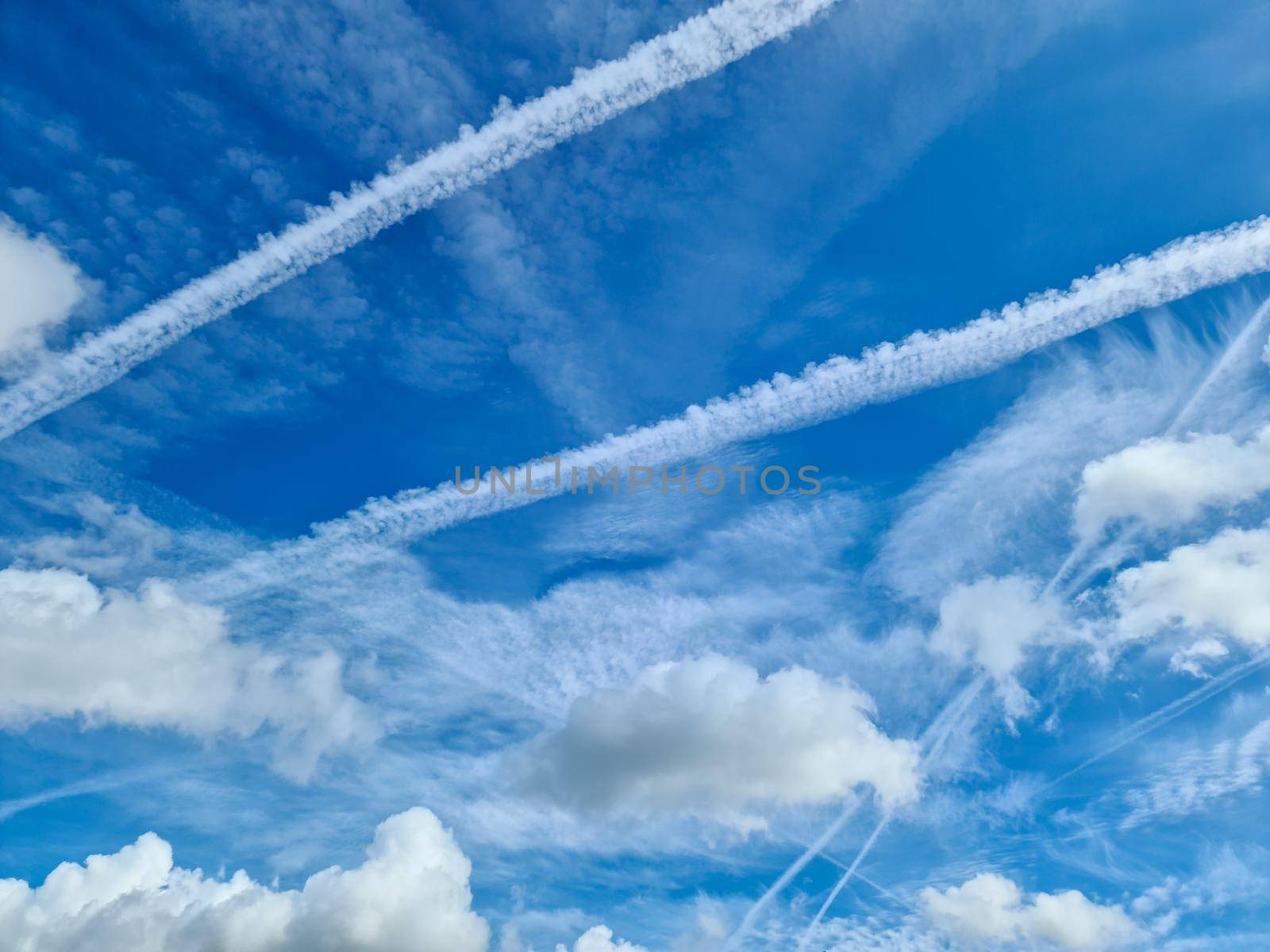Aircraft condensation contrails in the blue sky inbetween some beautiful clouds