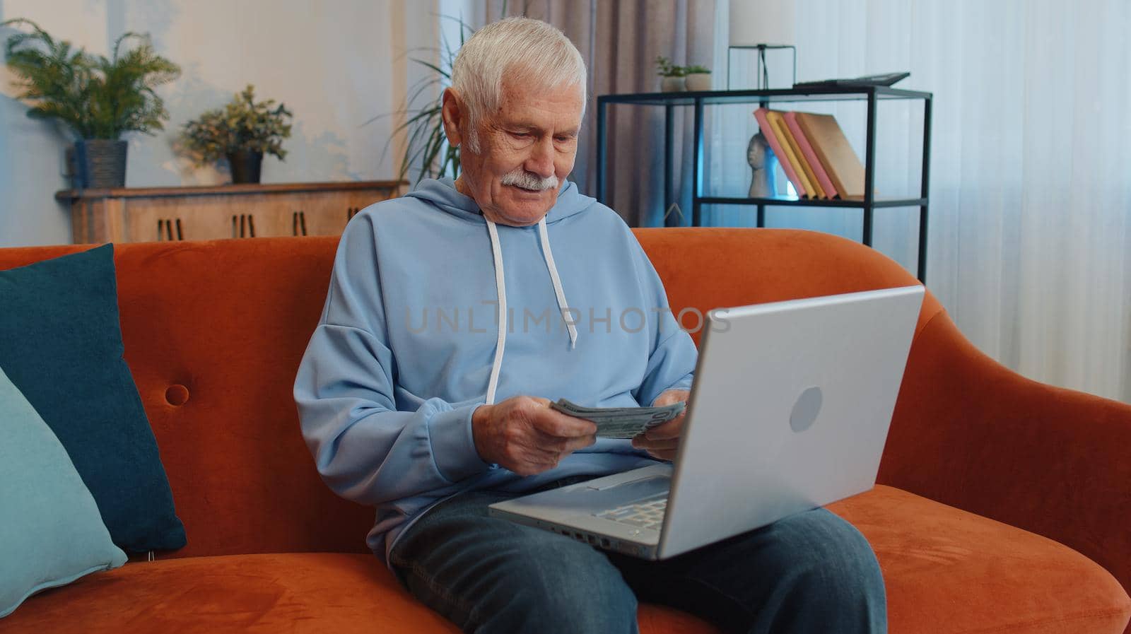 Planning budget. Rich happy senior grandfather counting money cash use laptop calculate domestic bills at home. Joyful elderly man satisfied of income earnings, saves money for planned vacation gifts