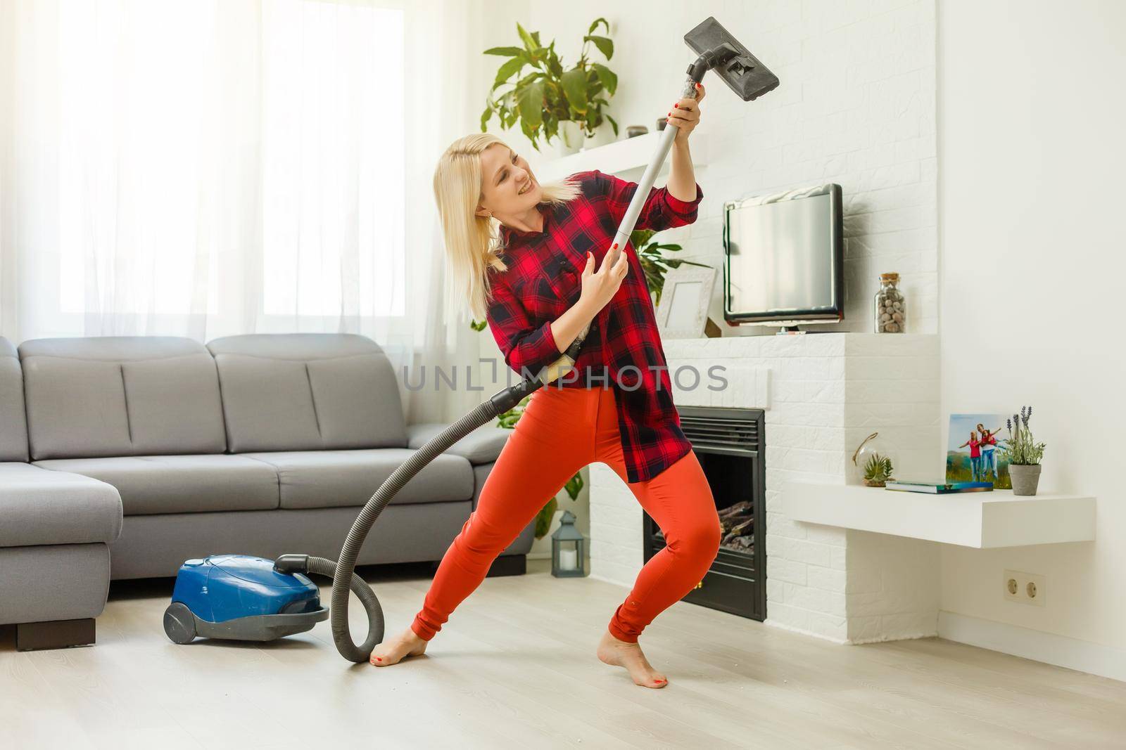 Smiling excited young housewife havig fun while cleaning floor with vacuum cleaner. Happy woman doing housework at home enjoy music wearing earphones. by Andelov13