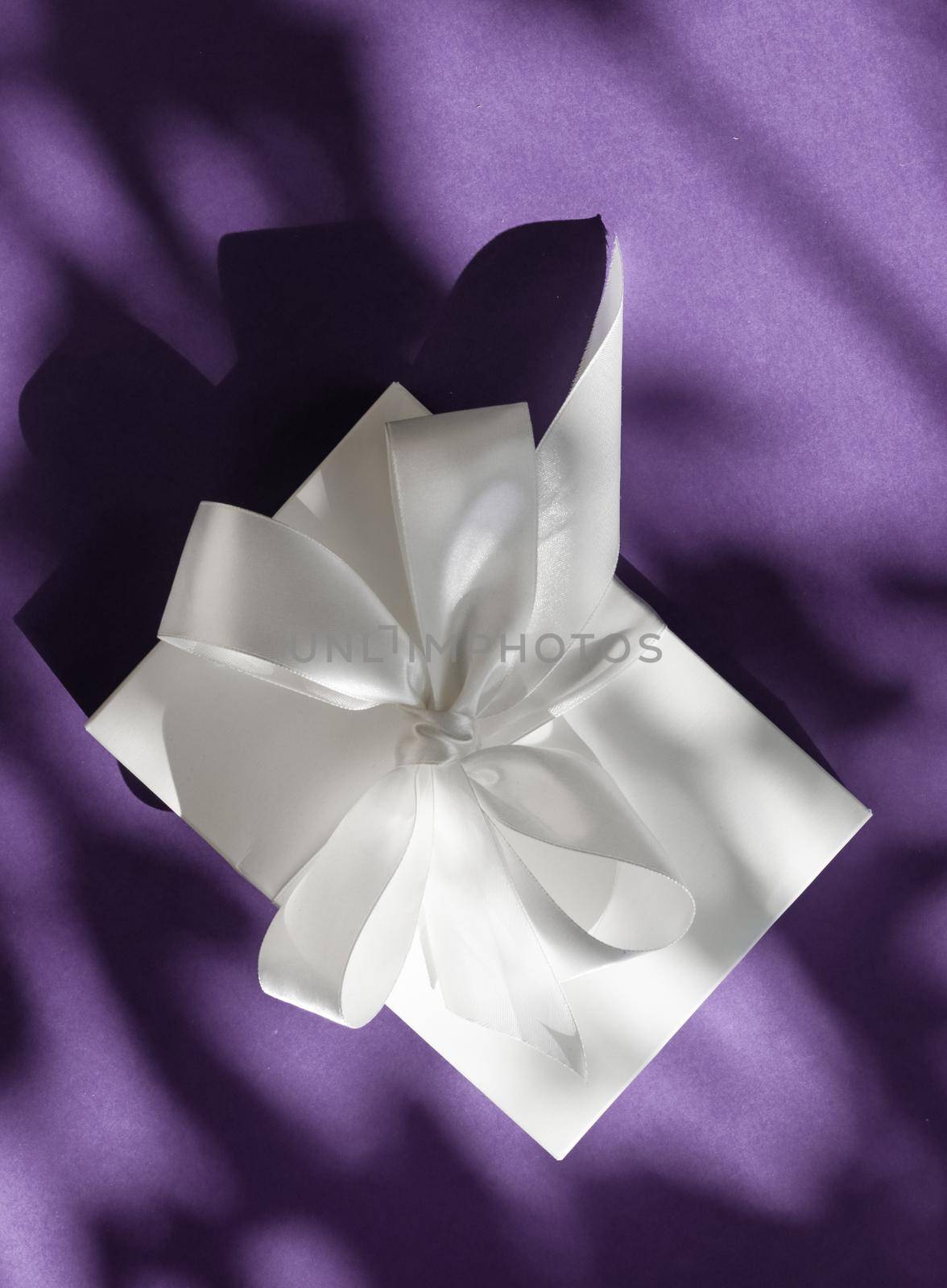 Luxury holiday white gift box with silk ribbon and bow on violet background, luxe wedding or birthday present by Anneleven