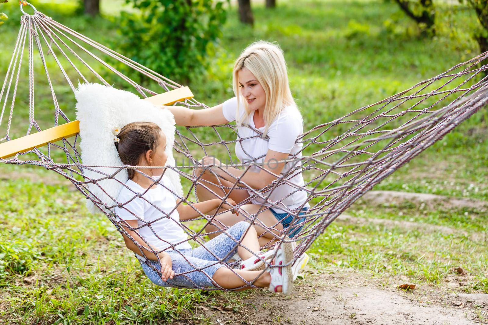 Happy mother and daughter relaxing together in a hammock at garden in sunny summer day. Family playing in hammock. by Andelov13