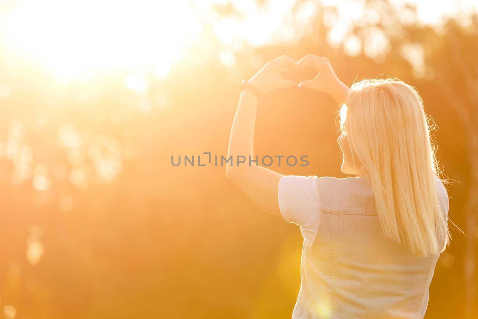 Female hands heart shape on nature green bokeh sun light flare and blur leaf abstract background. Happy love and freedom concept. Vintage tone color style.