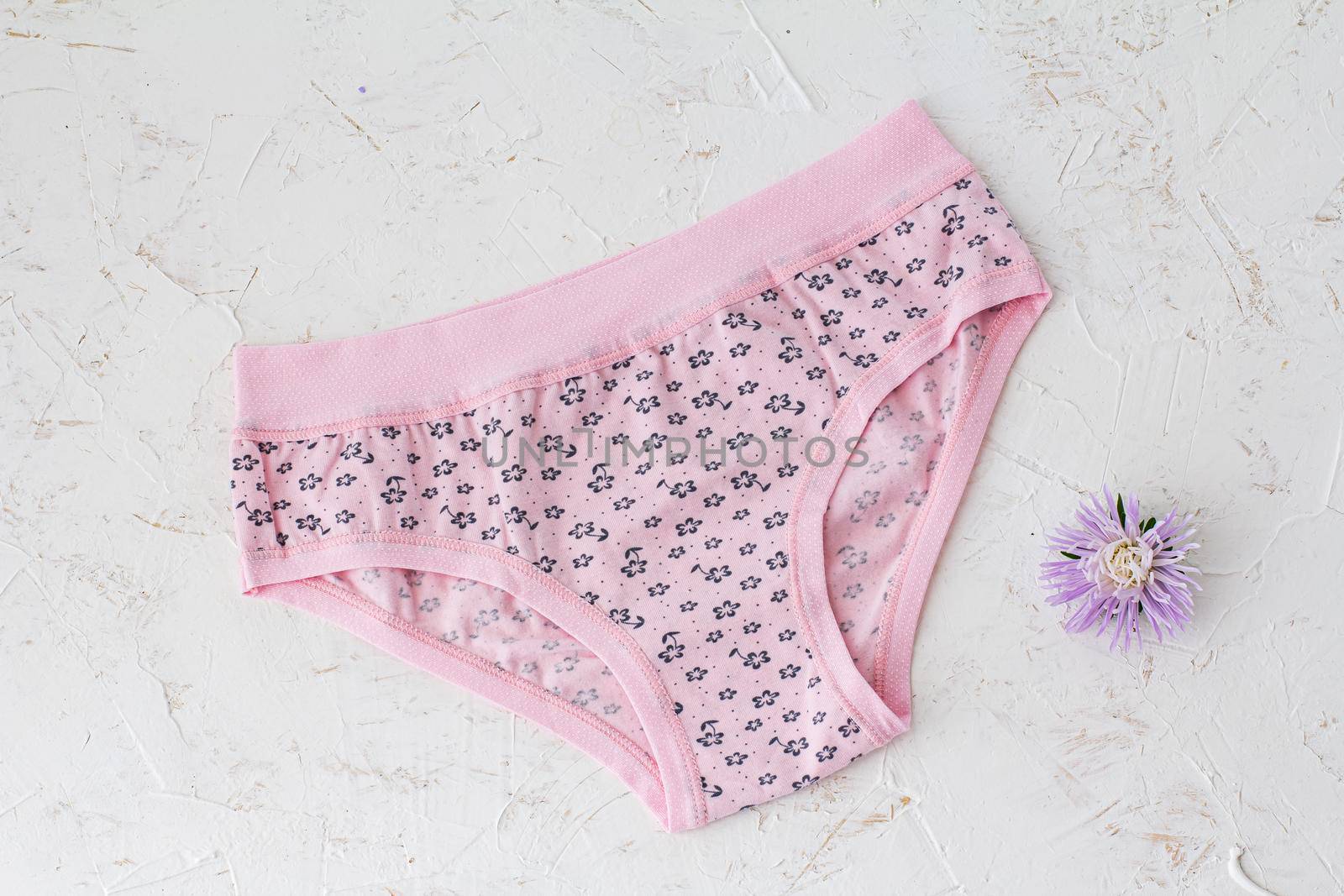 Pink cotton panties with flower bud on the white structured background. Woman underwear set. Top view.