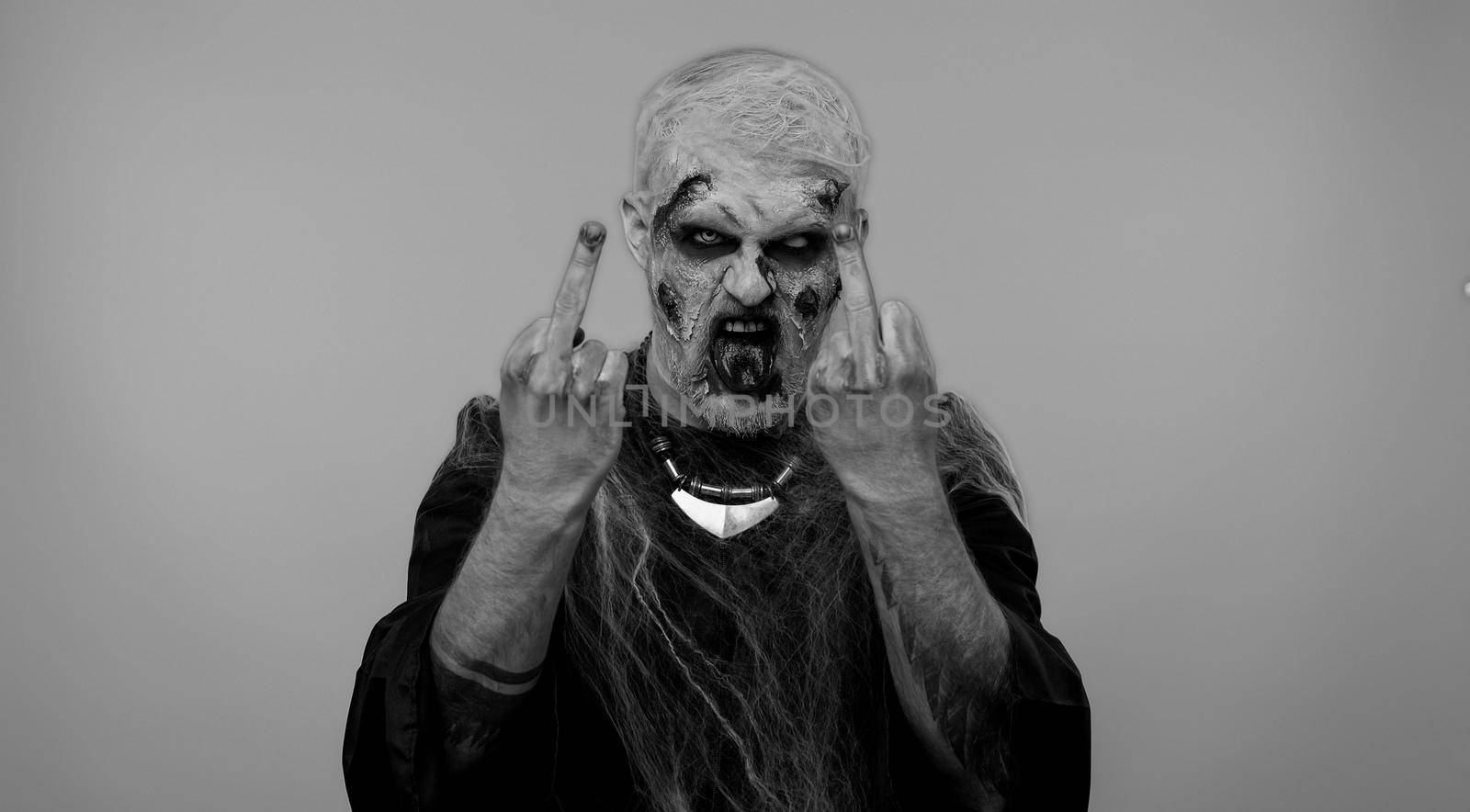 Aggressive crazy hooligan Halloween zombie man with makeup with wounds scars showing around his middle fingers, demonstrating protest with impolite rude gesture of disrespect, rejecting communication