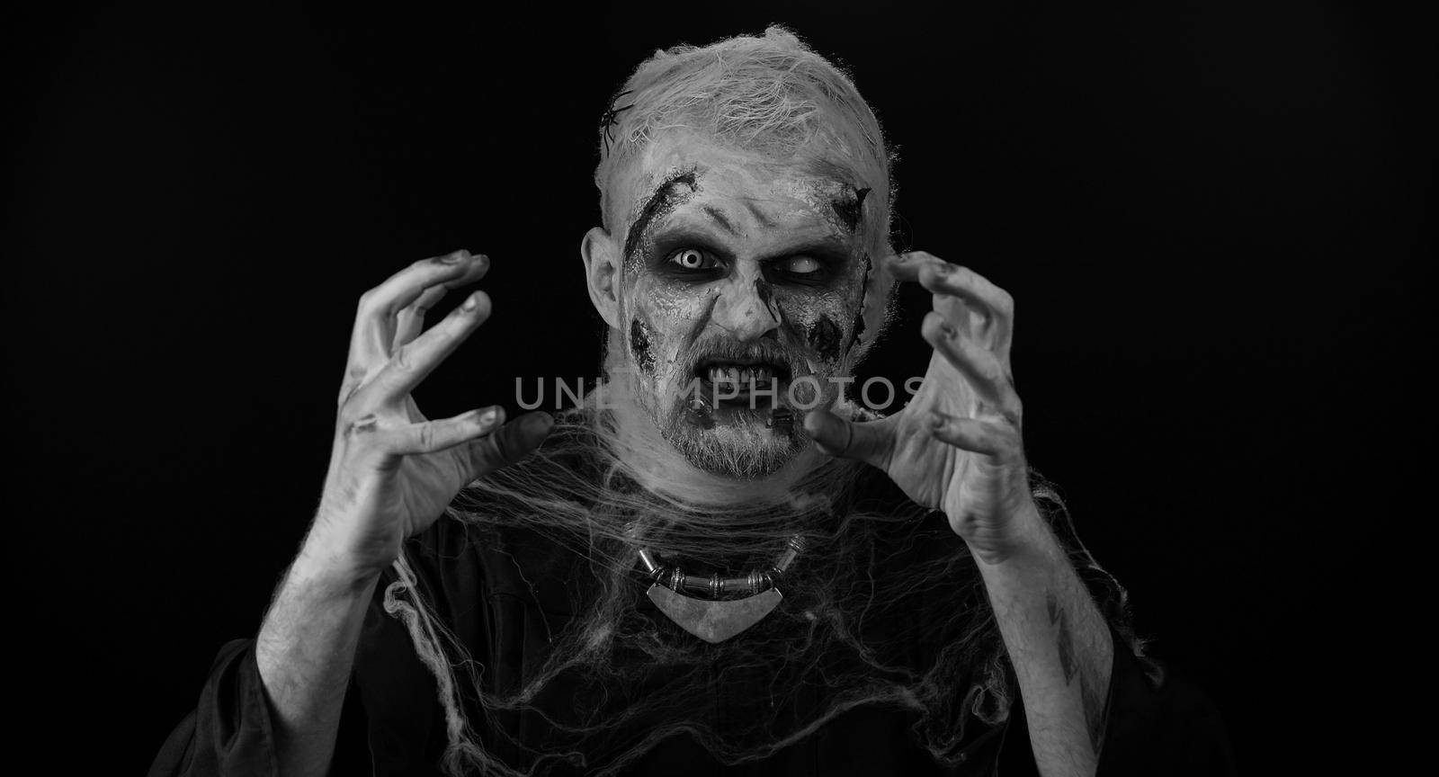 Portrait of sinister man in carnival costume of Halloween crazy zombie with bloody wounded scars face trying to scare isolated on black room. Horror theme of cosplay wounded undead, beast, monster