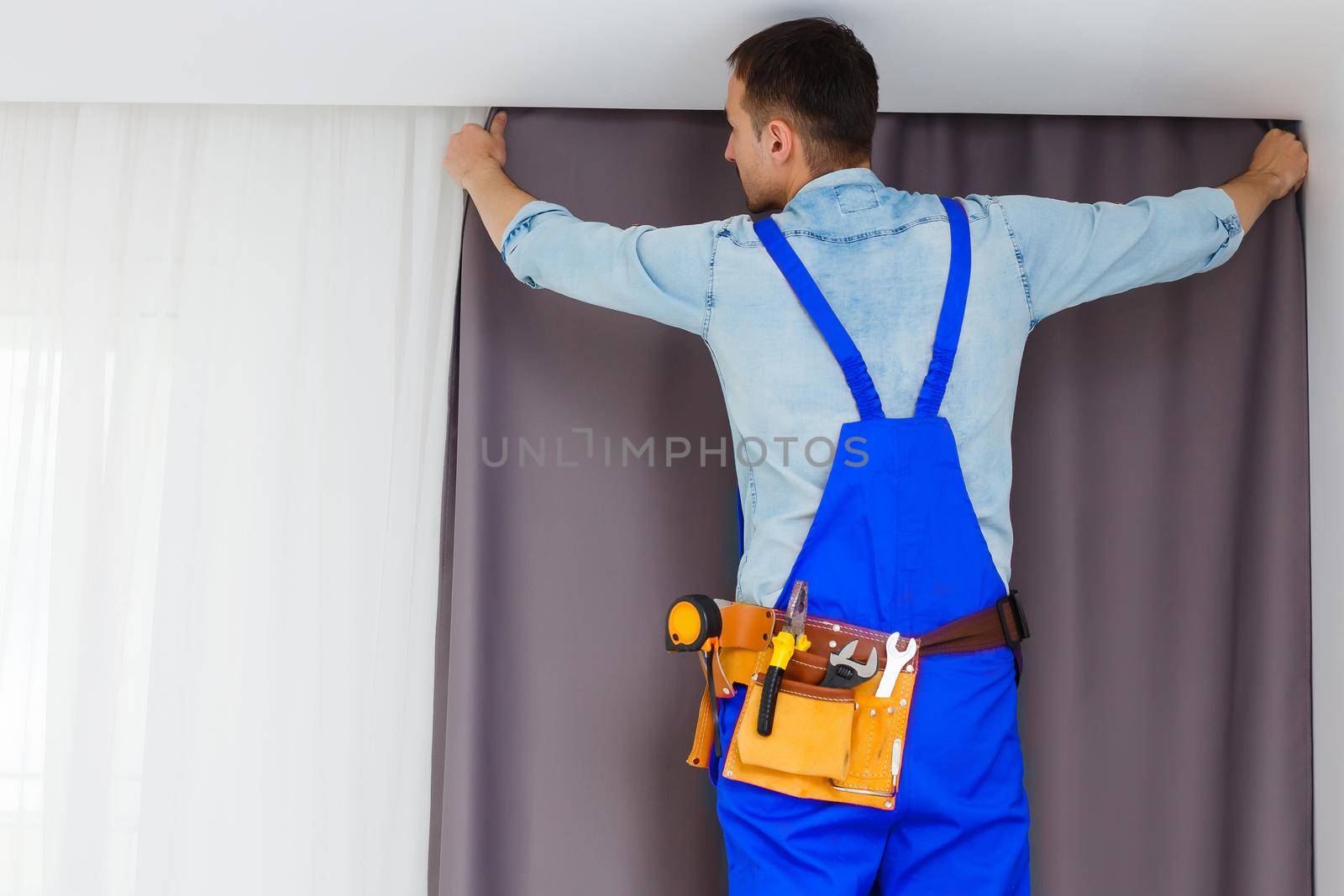 Young handsome man or handyman installing curtains over window at home, doing renovation work