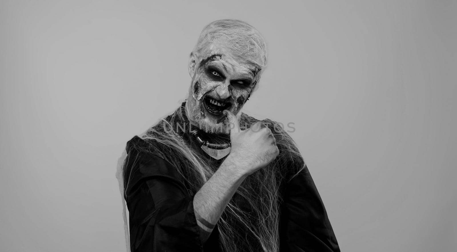 Creepy man with scary Halloween zombie makeup in costume raises thumbs up agrees with something or gives positive reply recommends advertisement likes good. Dead guy with wounded bloody scars face
