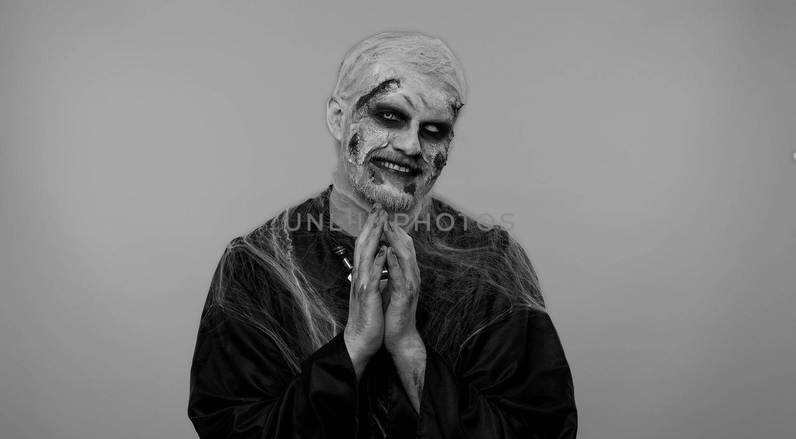 Sneaky cunning zombie man with makeup with wounds scars with tricky face gesticulating and scheming evil plan, thinking over devious villain idea, cunning cheats, jokes and pranks. Sinister dead guy