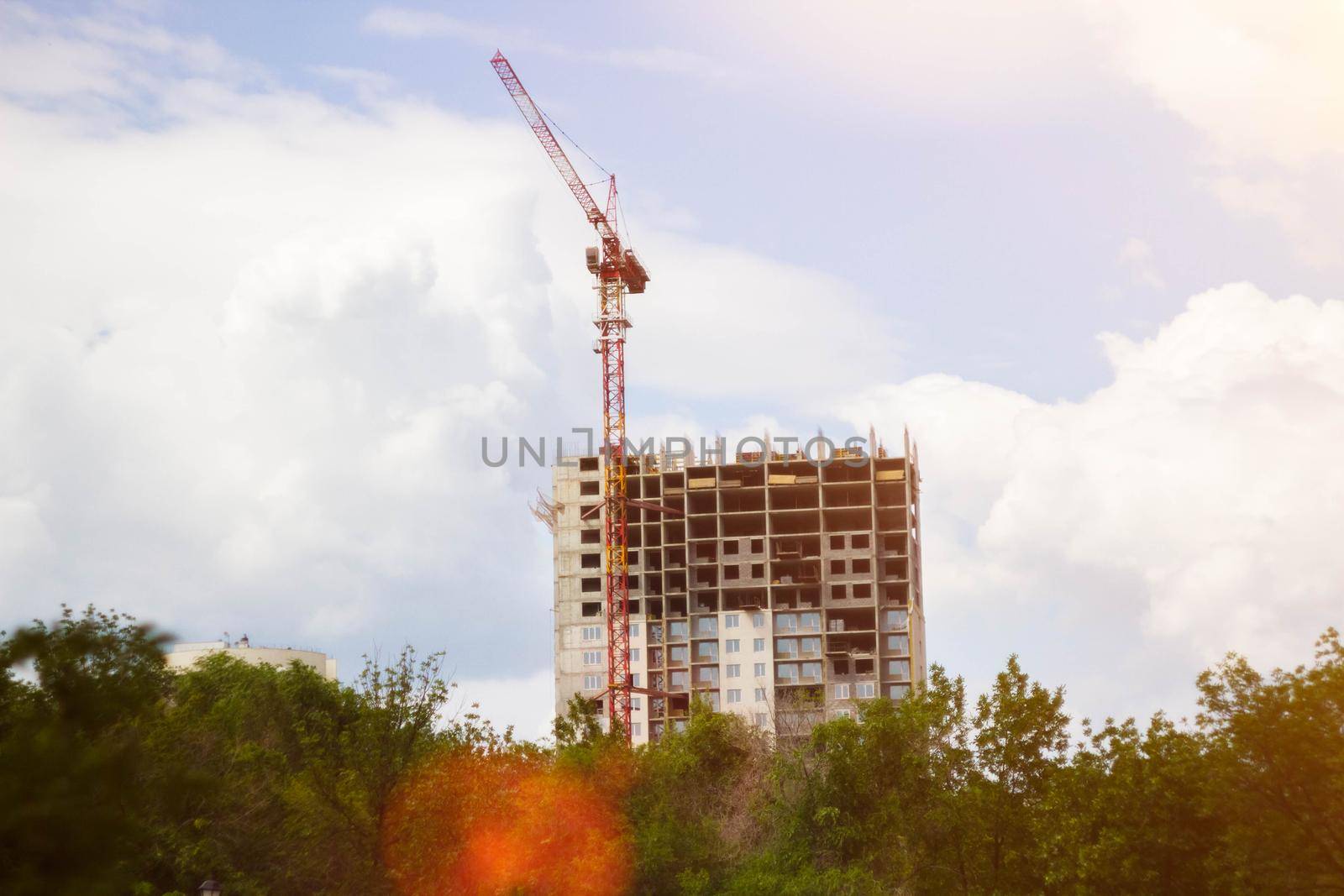 Construction crane in rays of bright sun. House under construction and crane. Construction site. Construction of new house.