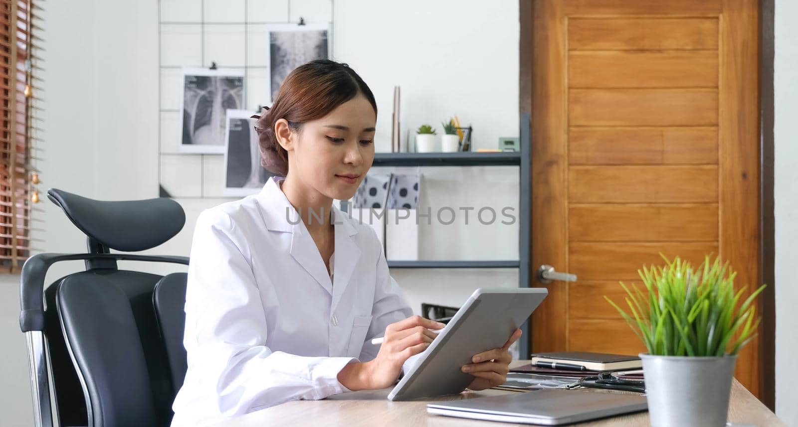 asian female doctor with laptop computer in her office. Friendly medical professional with tablet computer in clinic