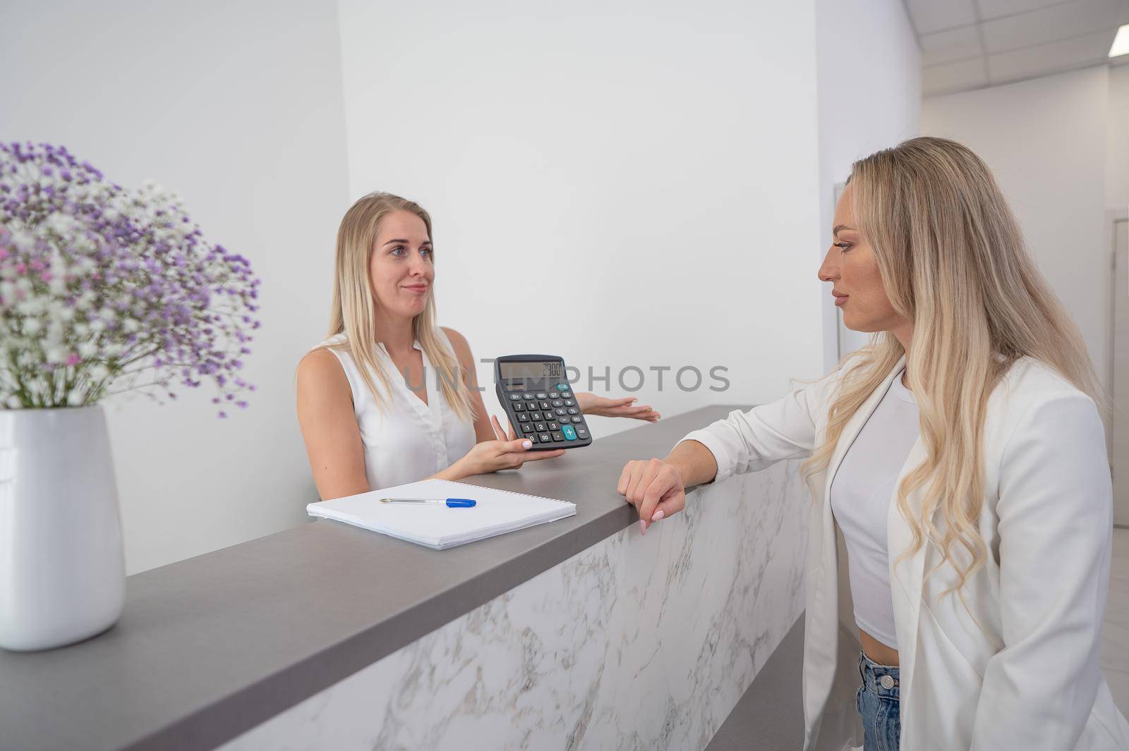 The administrator shows the client the amount on the calculator. Reception desk in a beauty salon