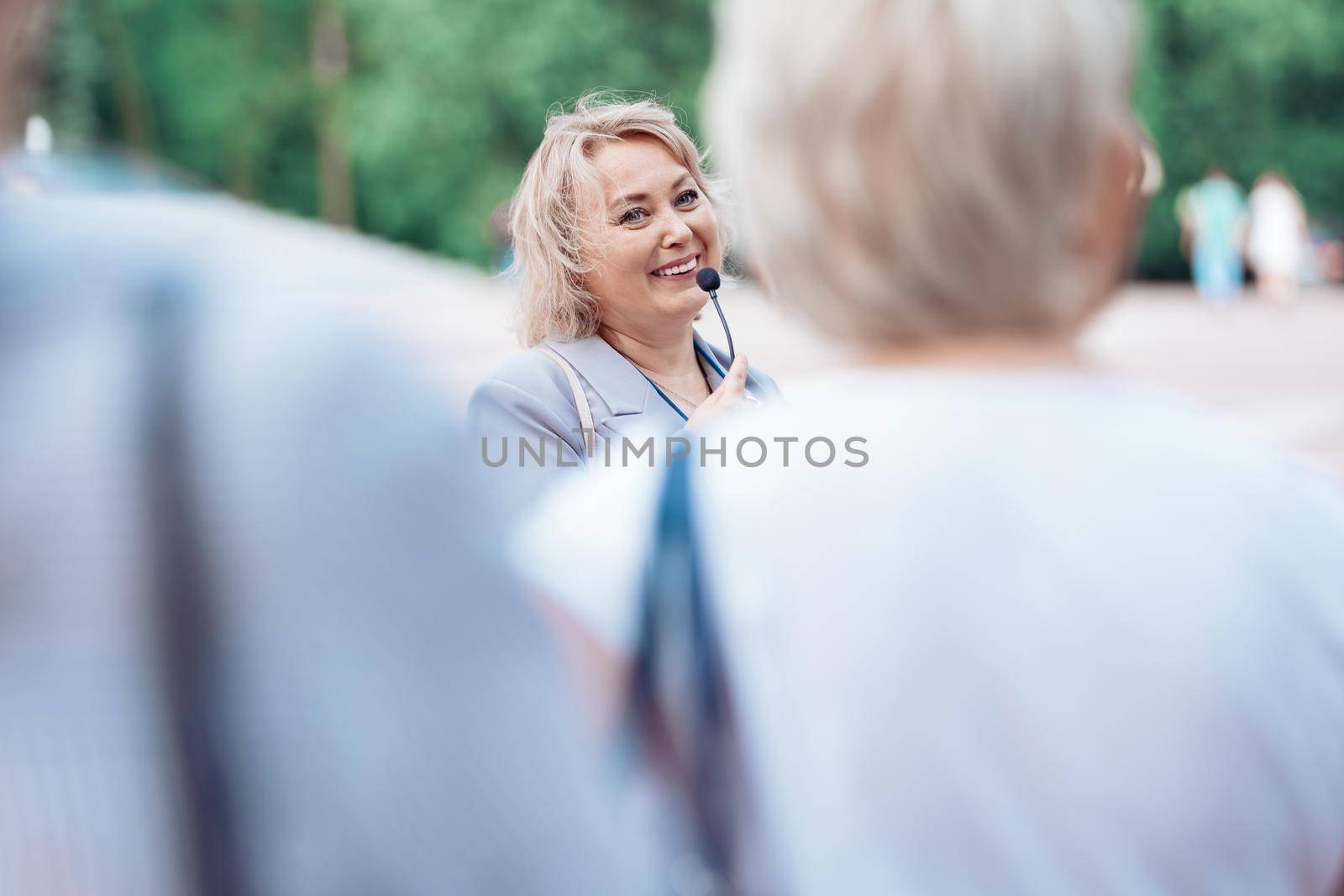 female tour guide with a microphone standing among a group of tourists. by SmartPhotoLab