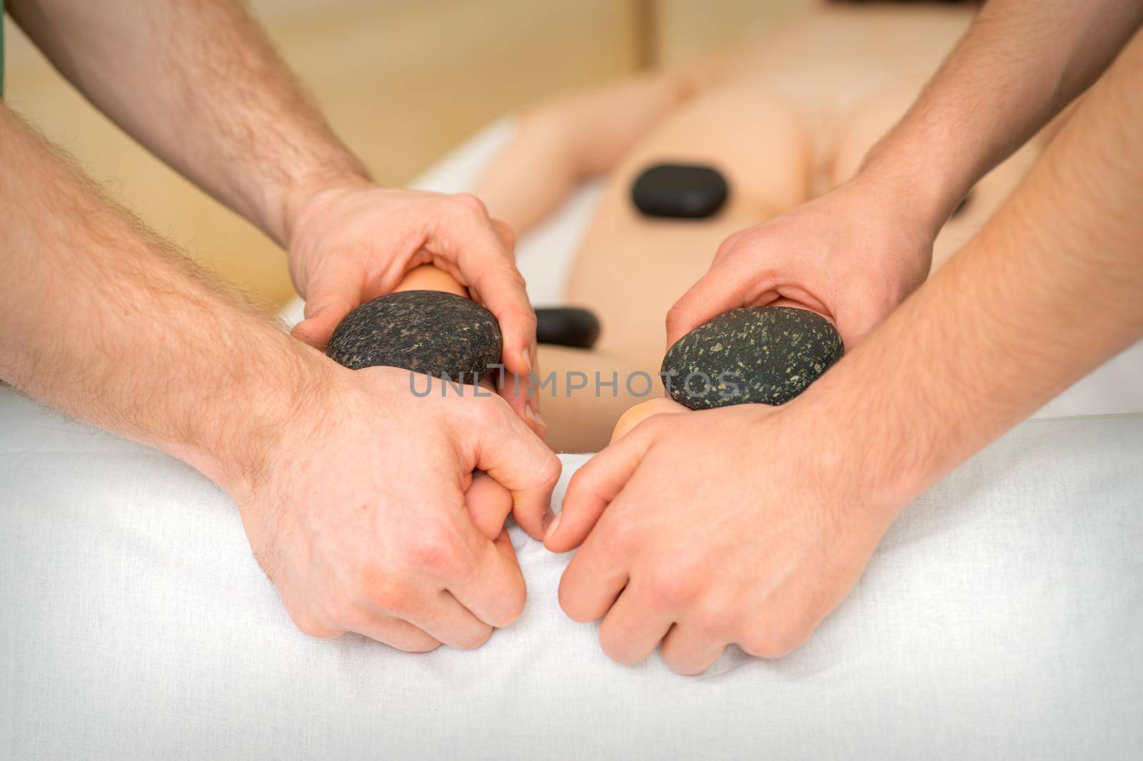 Two masseurs make a foot massage with a hot stone in four hands at the spa