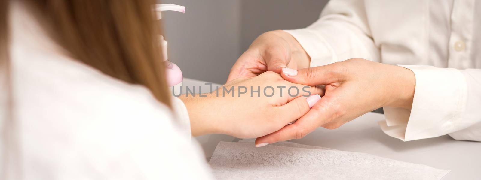 Manicure master massaging female hands before nail procedure in a nail salon. by okskukuruza