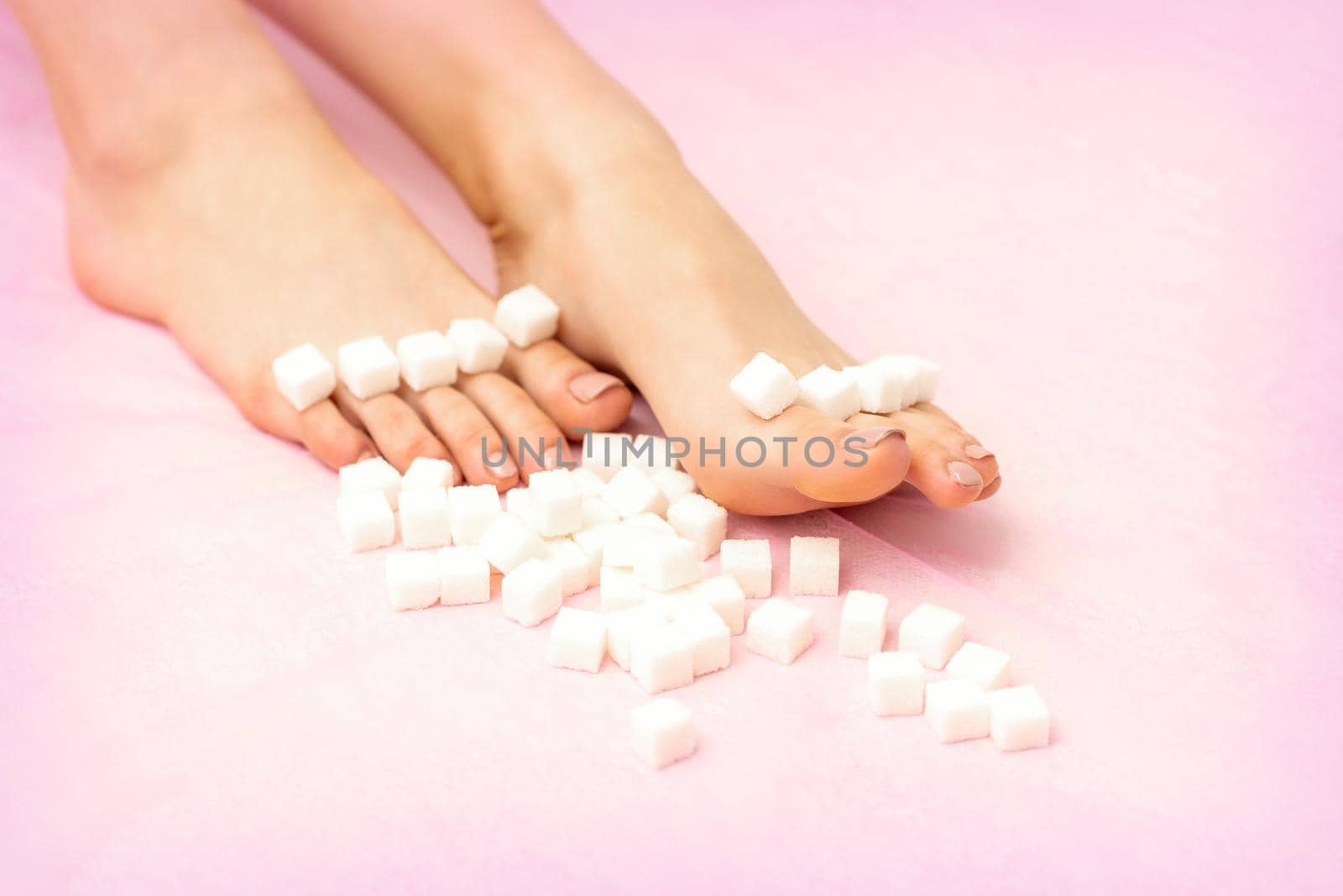 Sugar cubes lying in a row on female feet on pink background with copy space, depilation concept