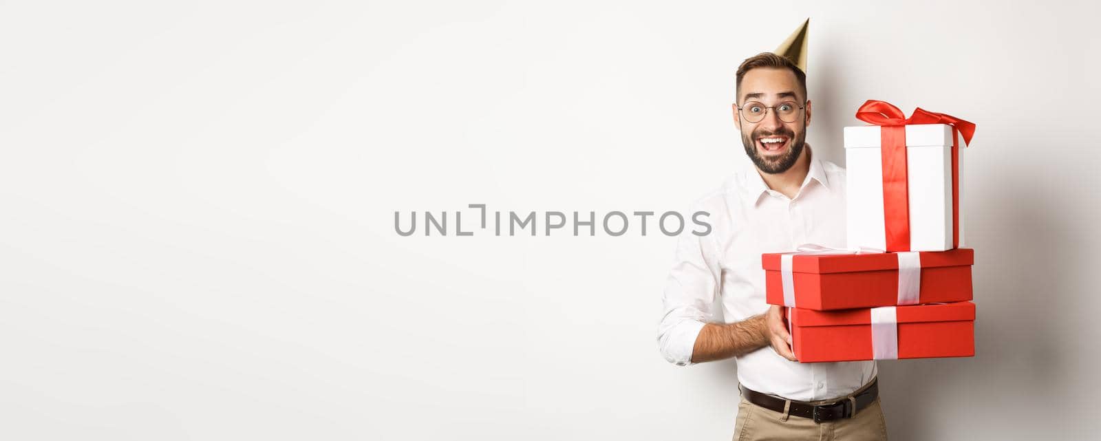 Holidays and celebration. Happy man receiving gifts on birthday, holding presents and looking excited, standing over white background.