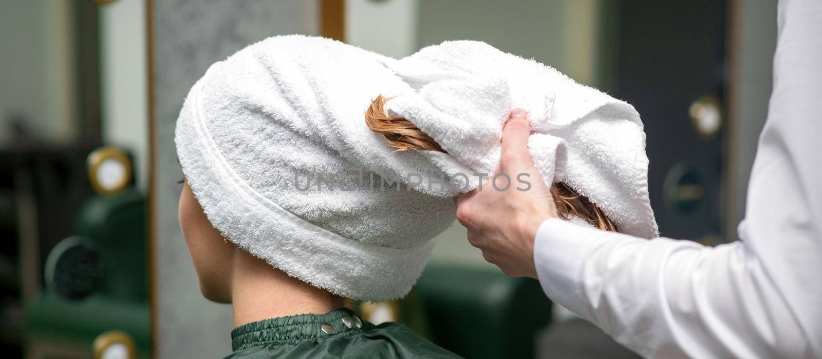 A hairdresser is wrapping the wet hair of the young woman in a towel after washing at the beauty salon. by okskukuruza