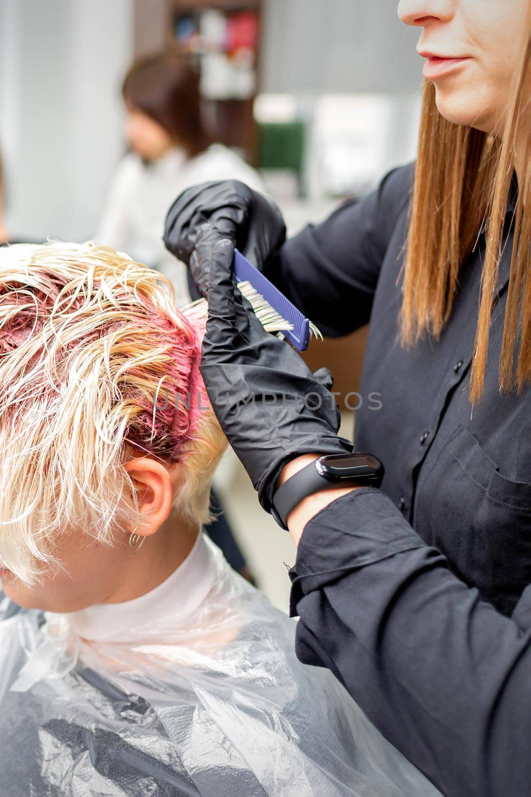 The professional hairdresser uses a brush to apply the pink dye to the hair. Hair coloring concept. by okskukuruza