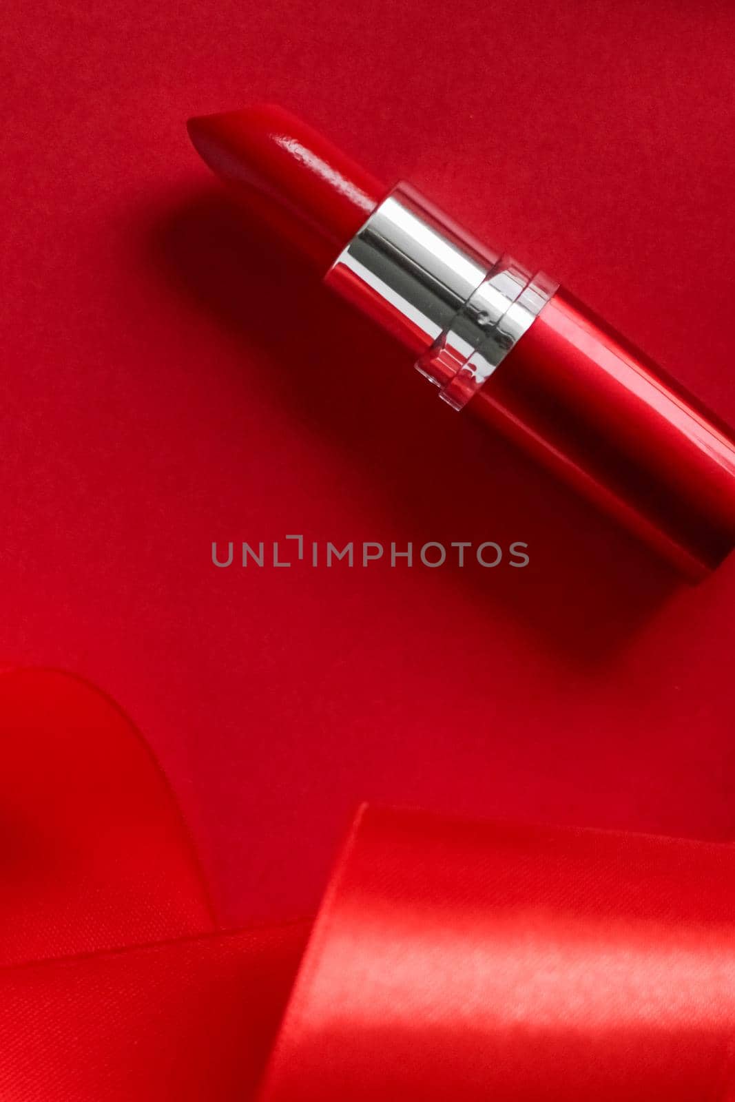 Cosmetic branding, glamour lip gloss and shopping sale concept - Luxury lipstick and silk ribbon on red holiday background, make-up and cosmetics flatlay for beauty brand product design
