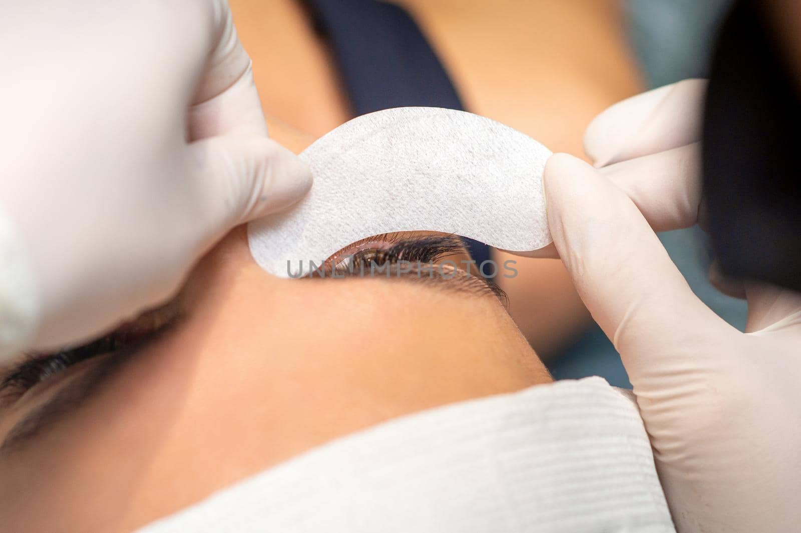 The beautician is gluing a patch under her eyes, before the procedure of eyelash extension. Artificial extended eyelashes