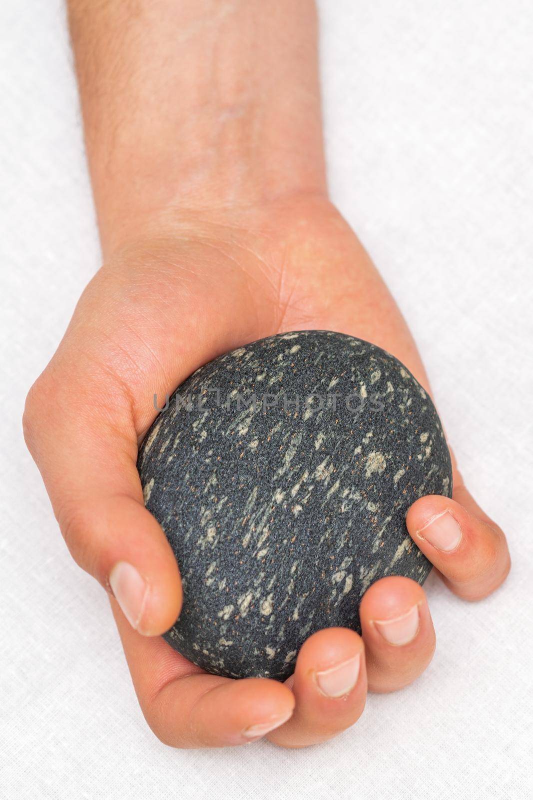 Hand of masseur holding massage stone on white background, top view