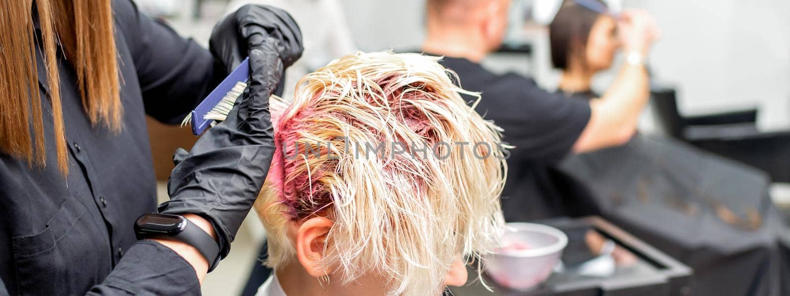 The professional hairdresser uses a brush to apply the pink dye to the hair. Hair coloring concept. by okskukuruza