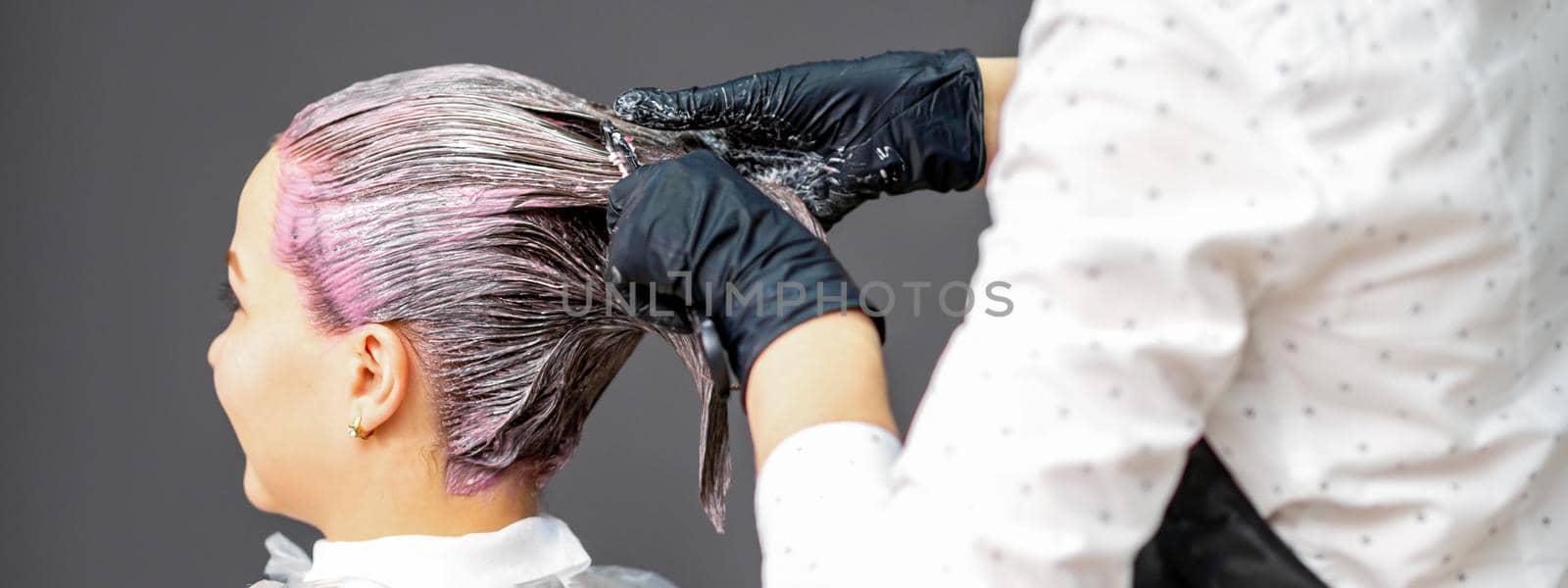 A hairdresser is applying color to the hair of a customer. Hair coloring in a beauty salon. Beauty and people concept. Close-up back view. by okskukuruza