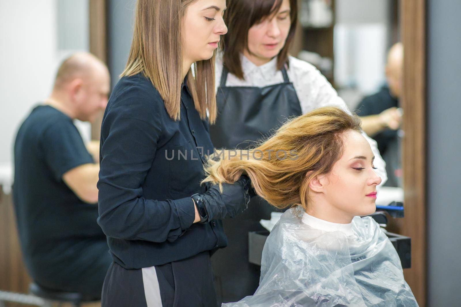 Two female hairstylists prepare long hair of a young woman making curls hairstyle in a beauty salon