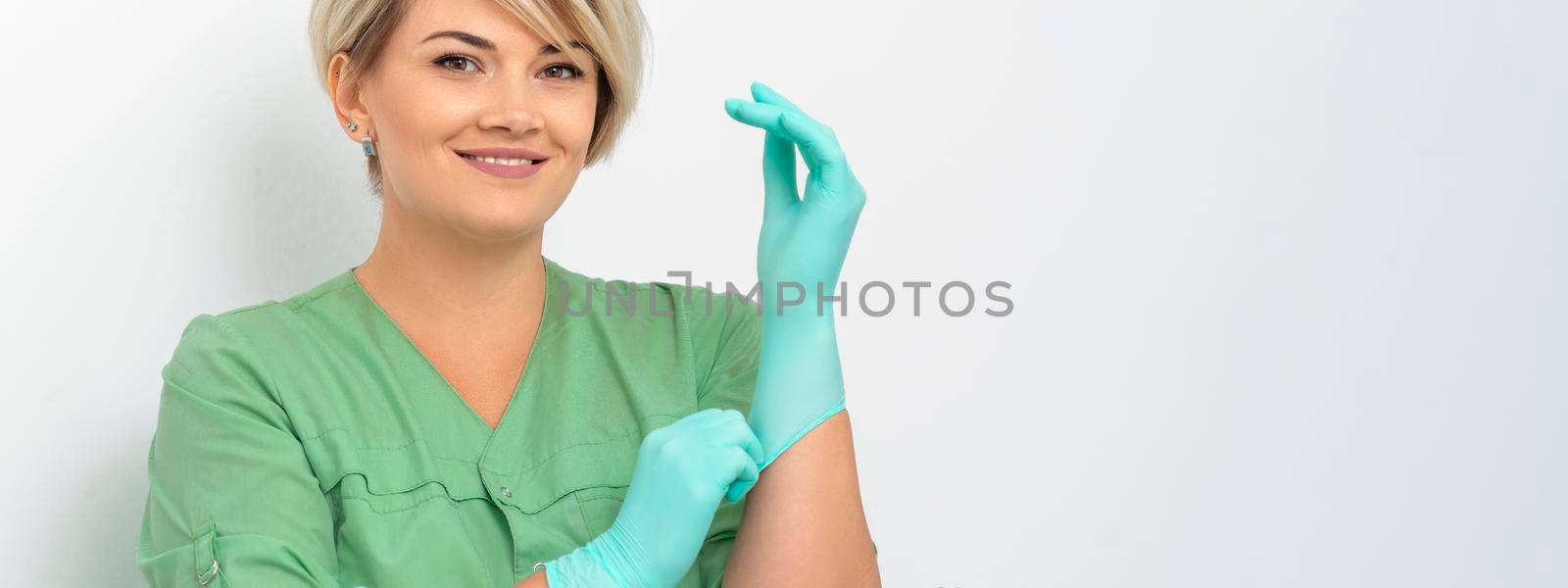 Doctor beautician puts on sterile blue gloves smiling prepares to receive clients on white