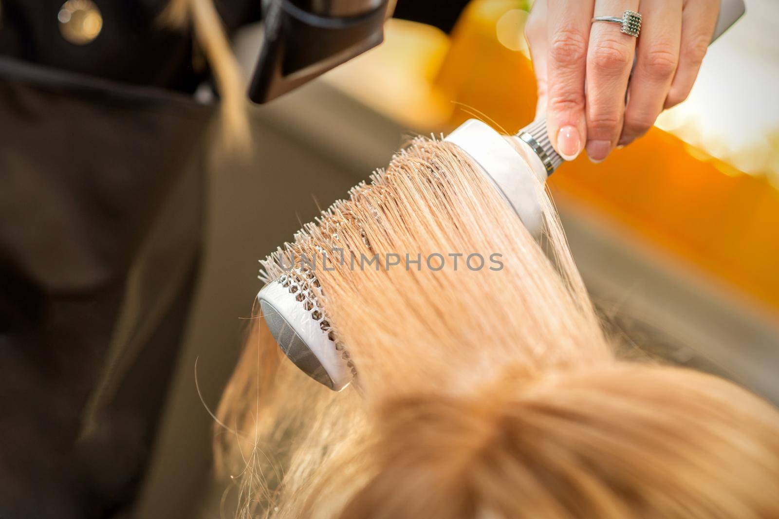 Hairdresser hand drying blond hair with a hairdryer and round brush in a beauty salon