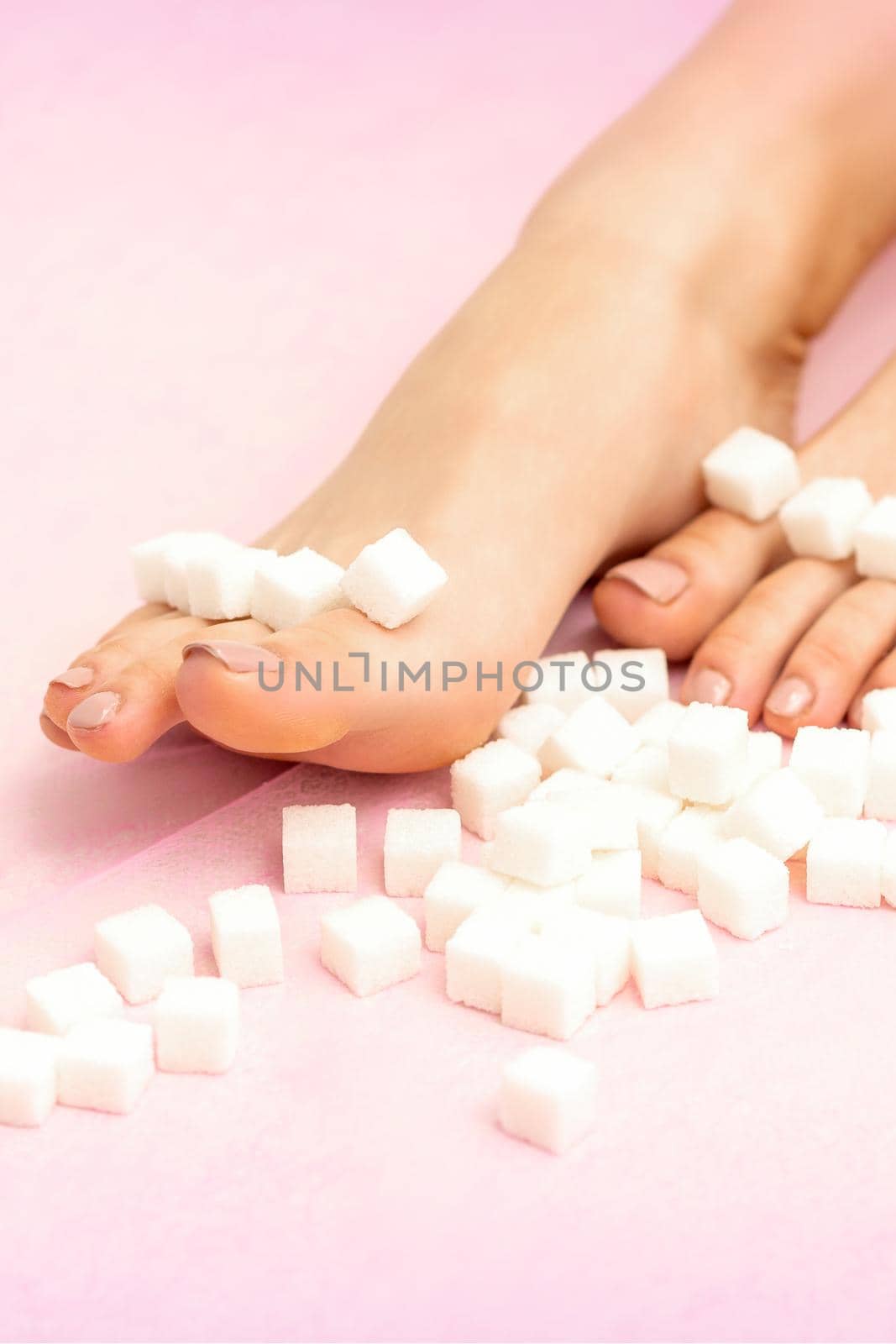 Sugar cubes lying in a row on female feet on pink background with copy space, depilation concept