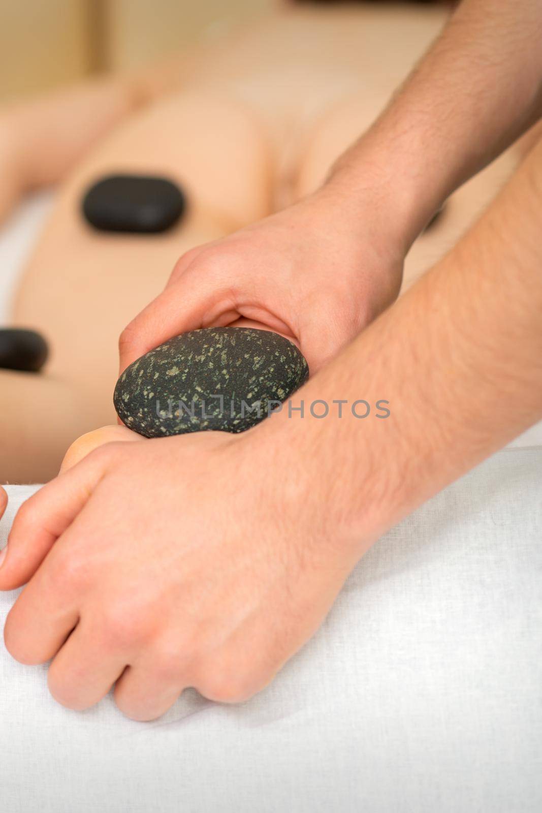 Two masseurs make a foot massage with a hot stone in four hands at the spa