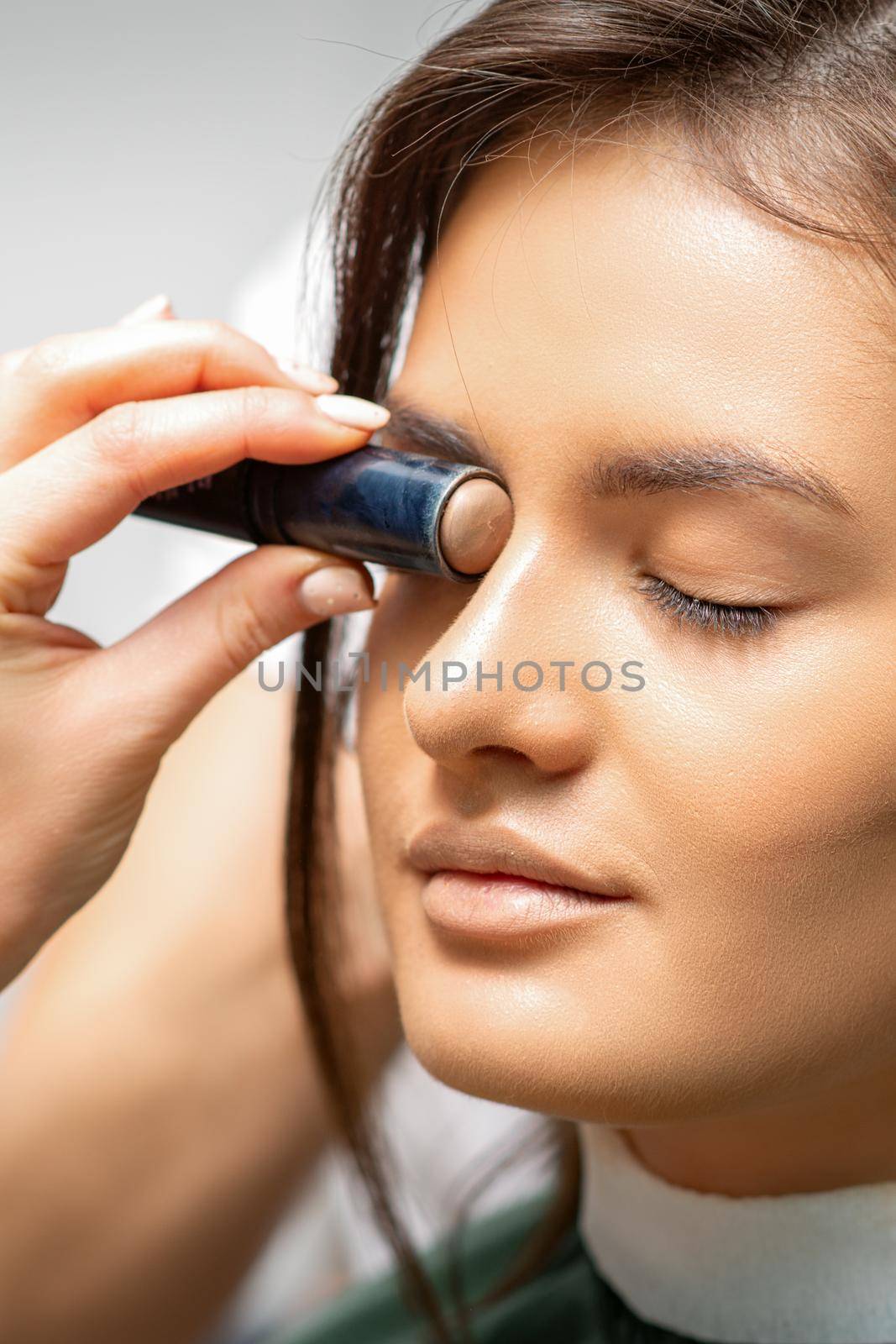 Make up artist contouring the face of a young woman with cream blush close up