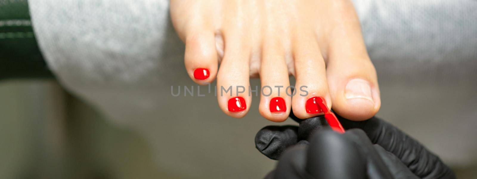 Pedicurist applying red nail polish to the female toenails in a beauty salon. by okskukuruza