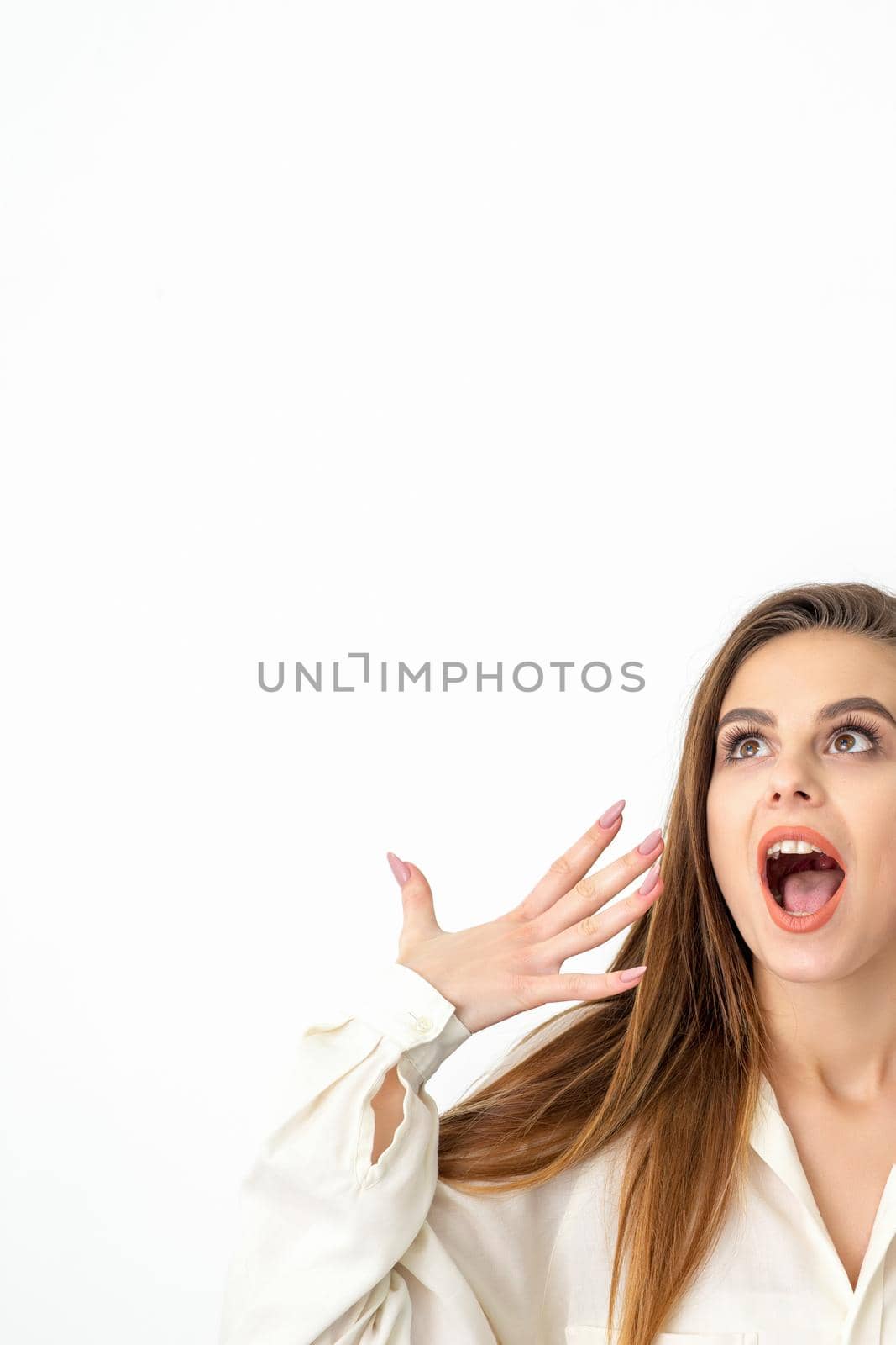 Shocked young caucasian woman with open mouth looking up and expresses surprise isolated over white background. Beautiful surprised brunette woman in studio. by okskukuruza