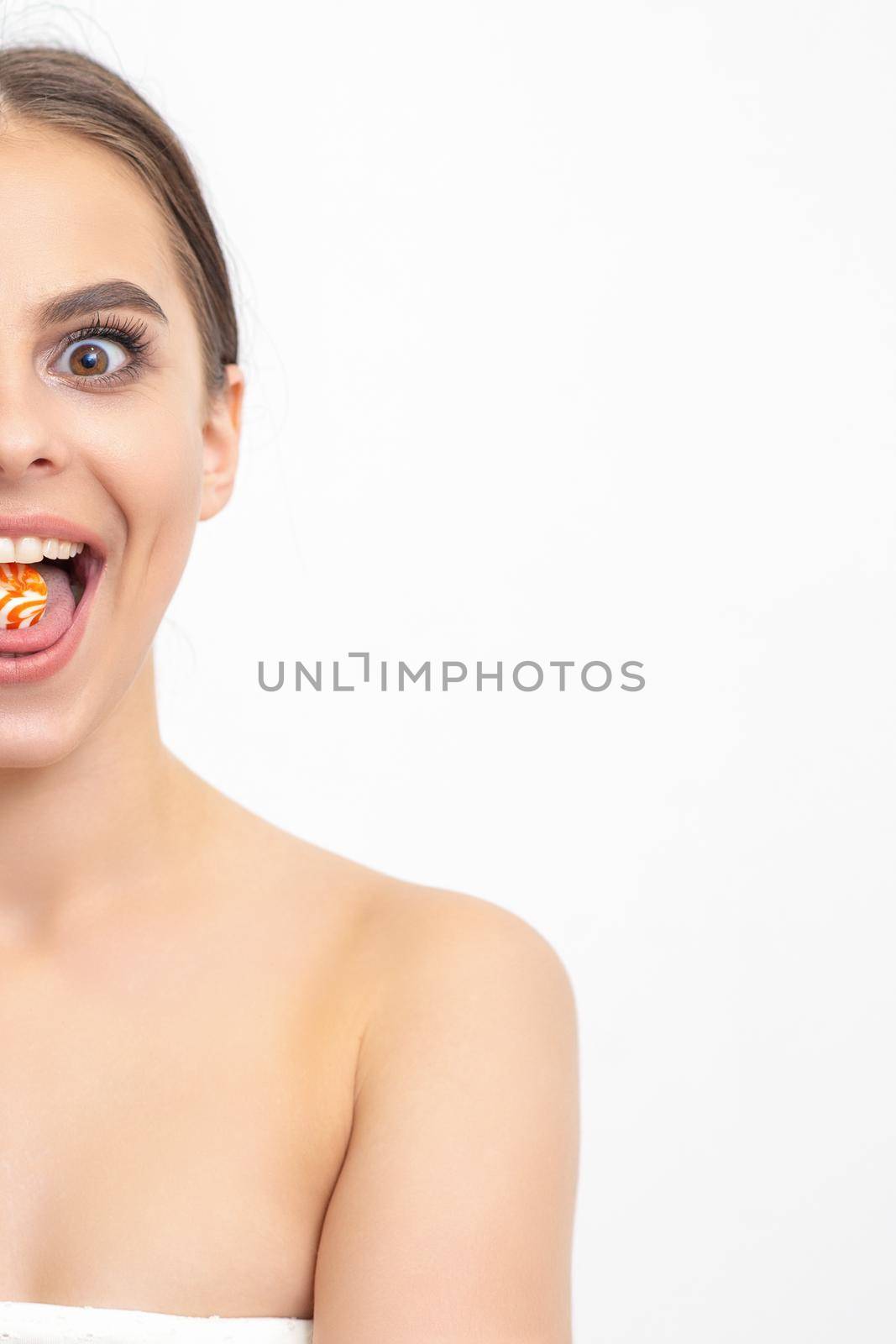 Happy expression young nude woman with candy in mouth on white background, epilation, depilation, hair removal concept. by okskukuruza