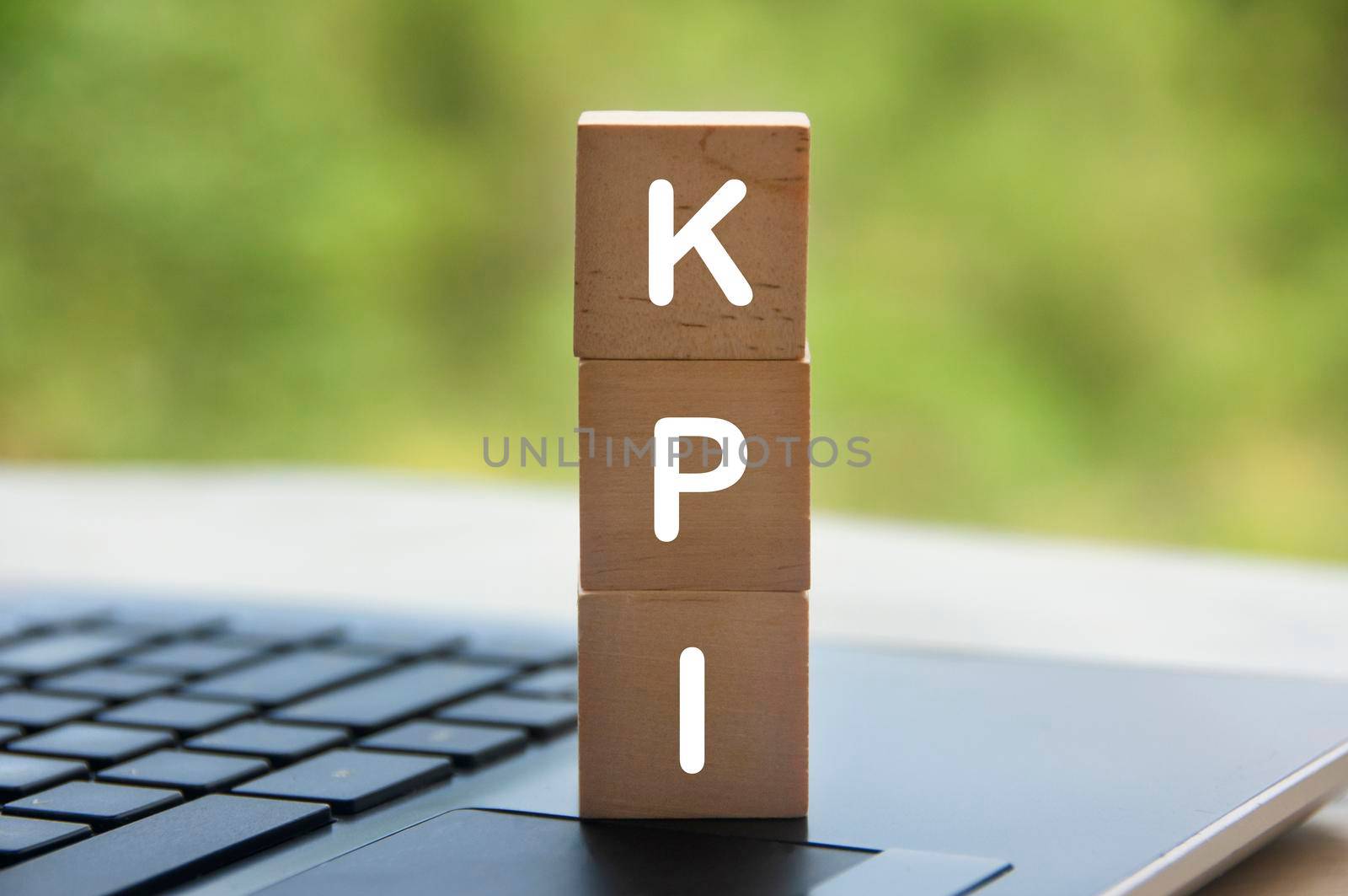 KPI text on wooden blocks with laptop and blurred nature background. Business and key performance indicator concept.