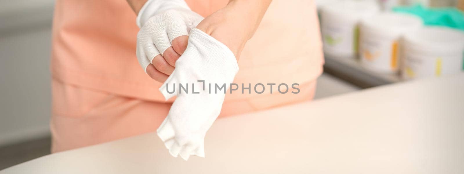 Cosmetologist in workwear wearing white bamboo fingerless gloves on her hands