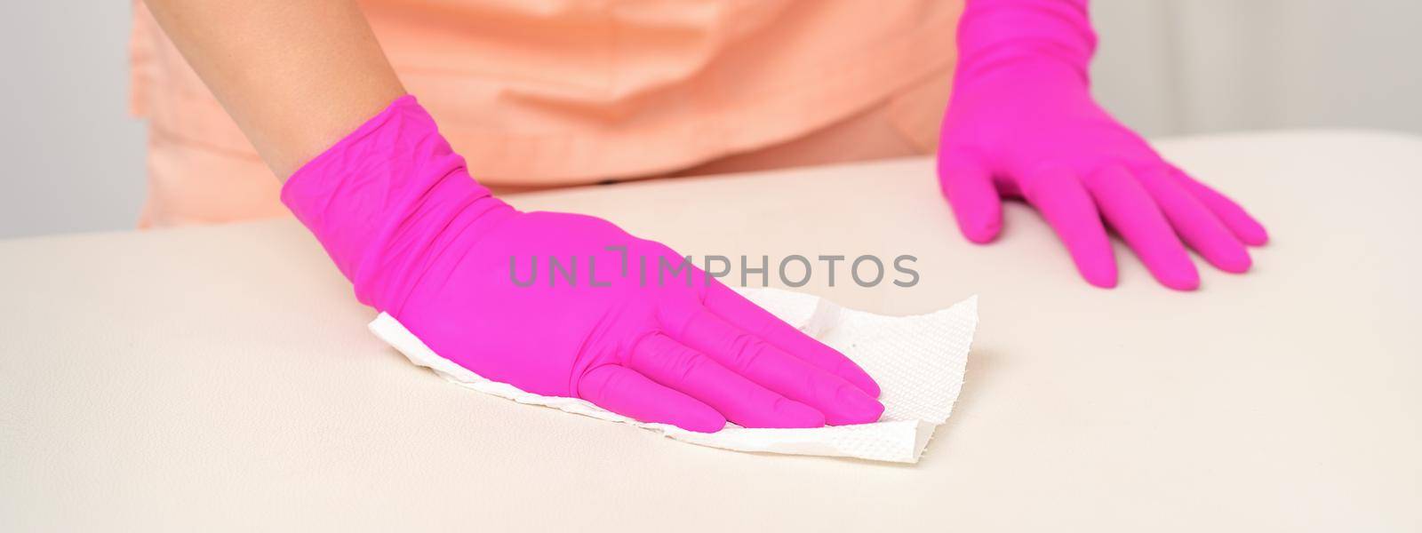 Close up of hands in rubber protective pink gloves cleaning the white surface with a white rag
