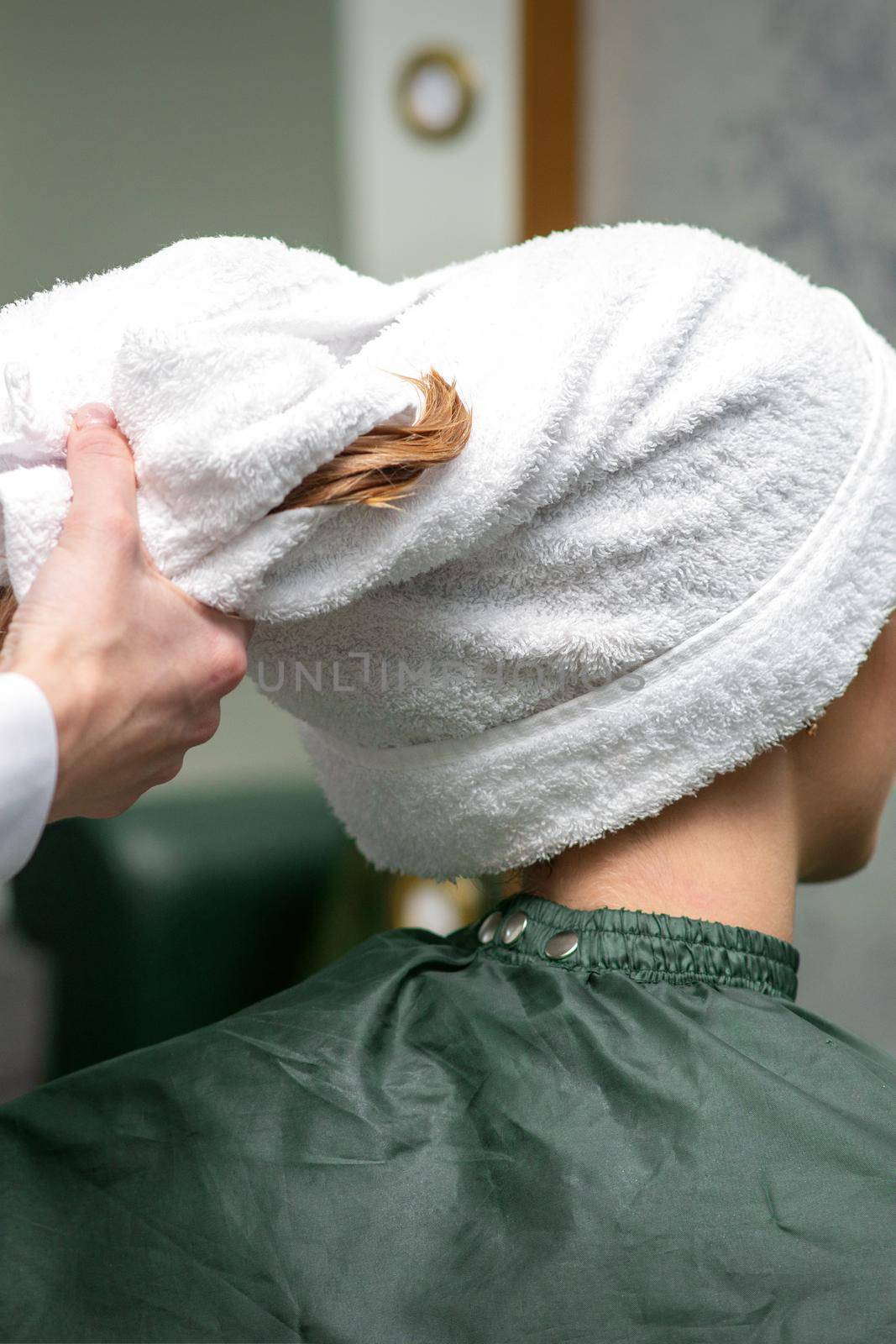 A hairdresser is wrapping the wet hair of the young woman in a towel after washing at the beauty salon