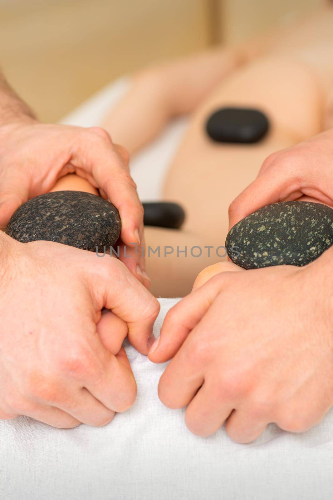 Two masseurs make a foot massage with a hot stone in four hands at the spa