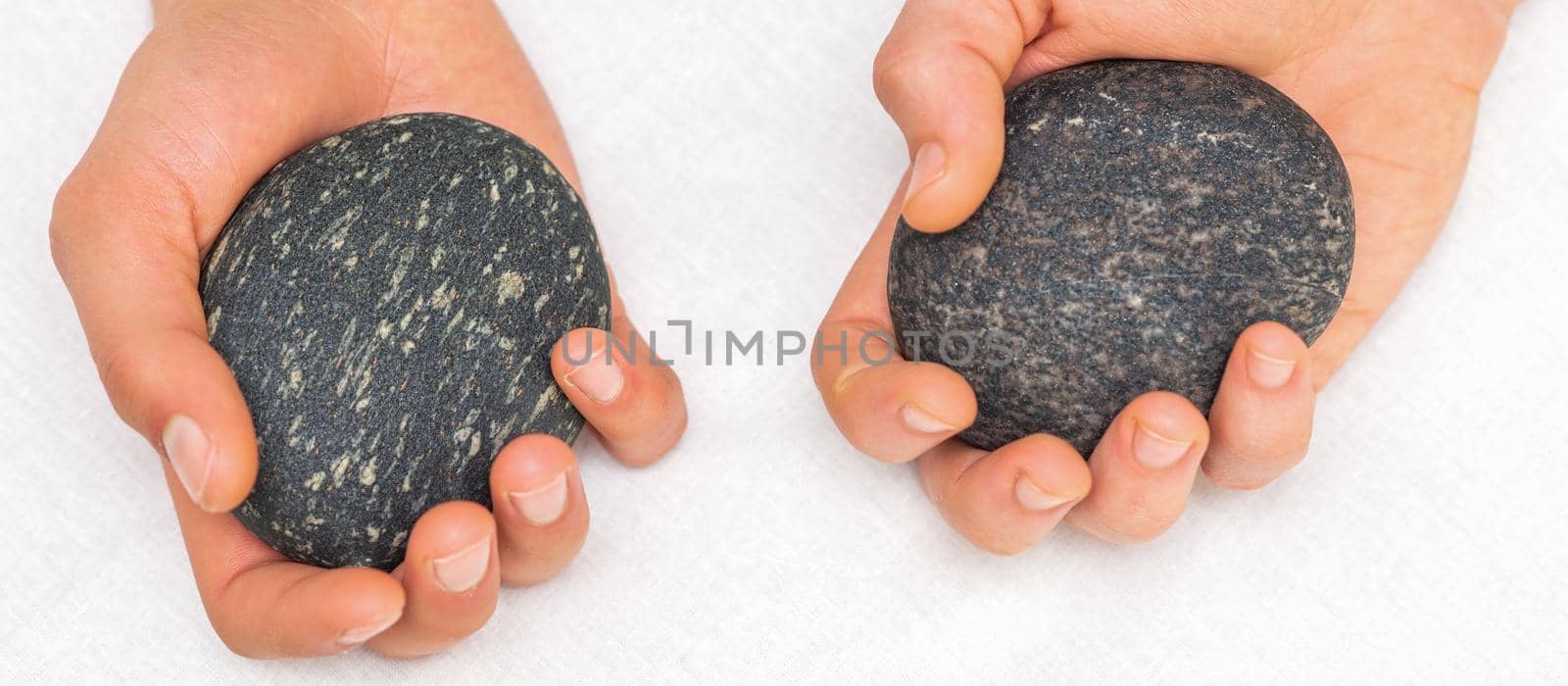 Hands of masseur holding massage stones on white background, top view