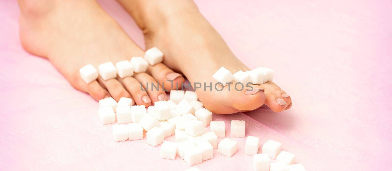Sugar cubes lying in a row on female feet on pink background with copy space, depilation concept