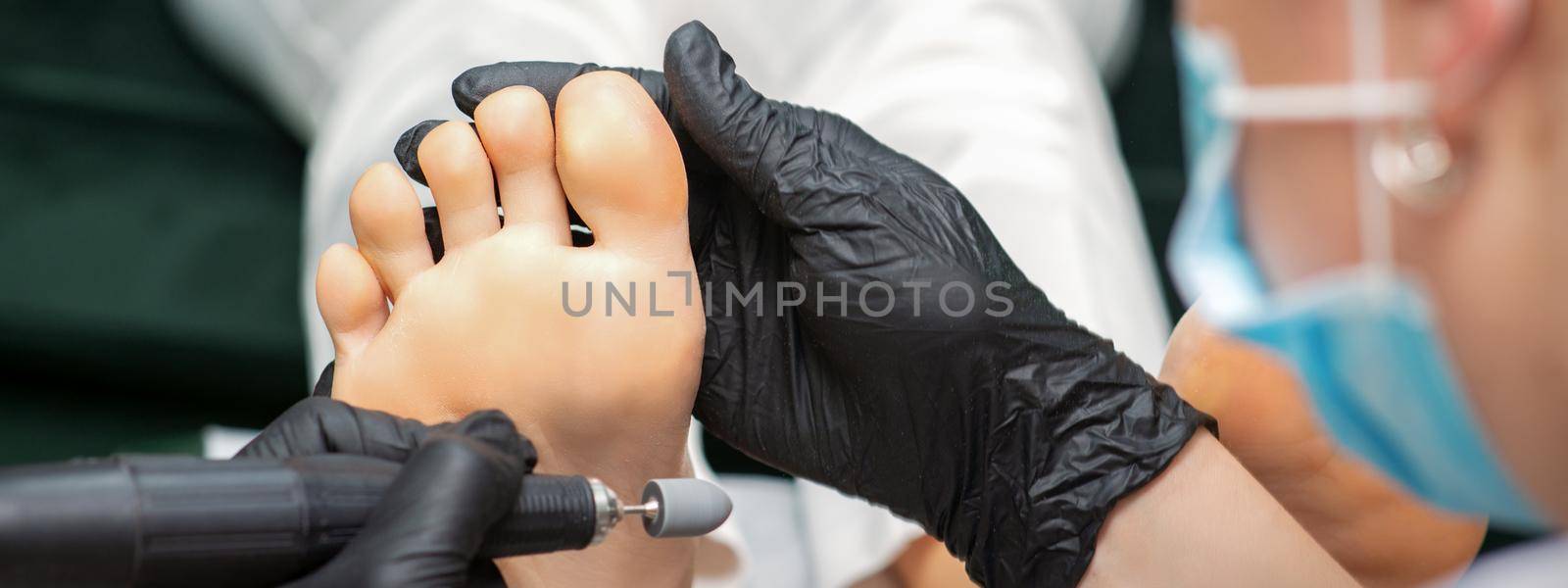 Peeling pedicure procedure on the sole from callus of the female foot by a pedicurist at a beauty salon