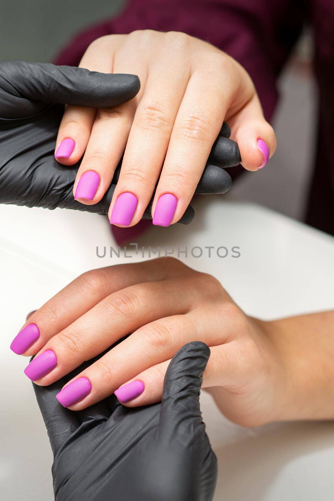 Examination of manicured fingernails. Hands of manicure master in black gloves examining female pink nails in manicure salon. by okskukuruza