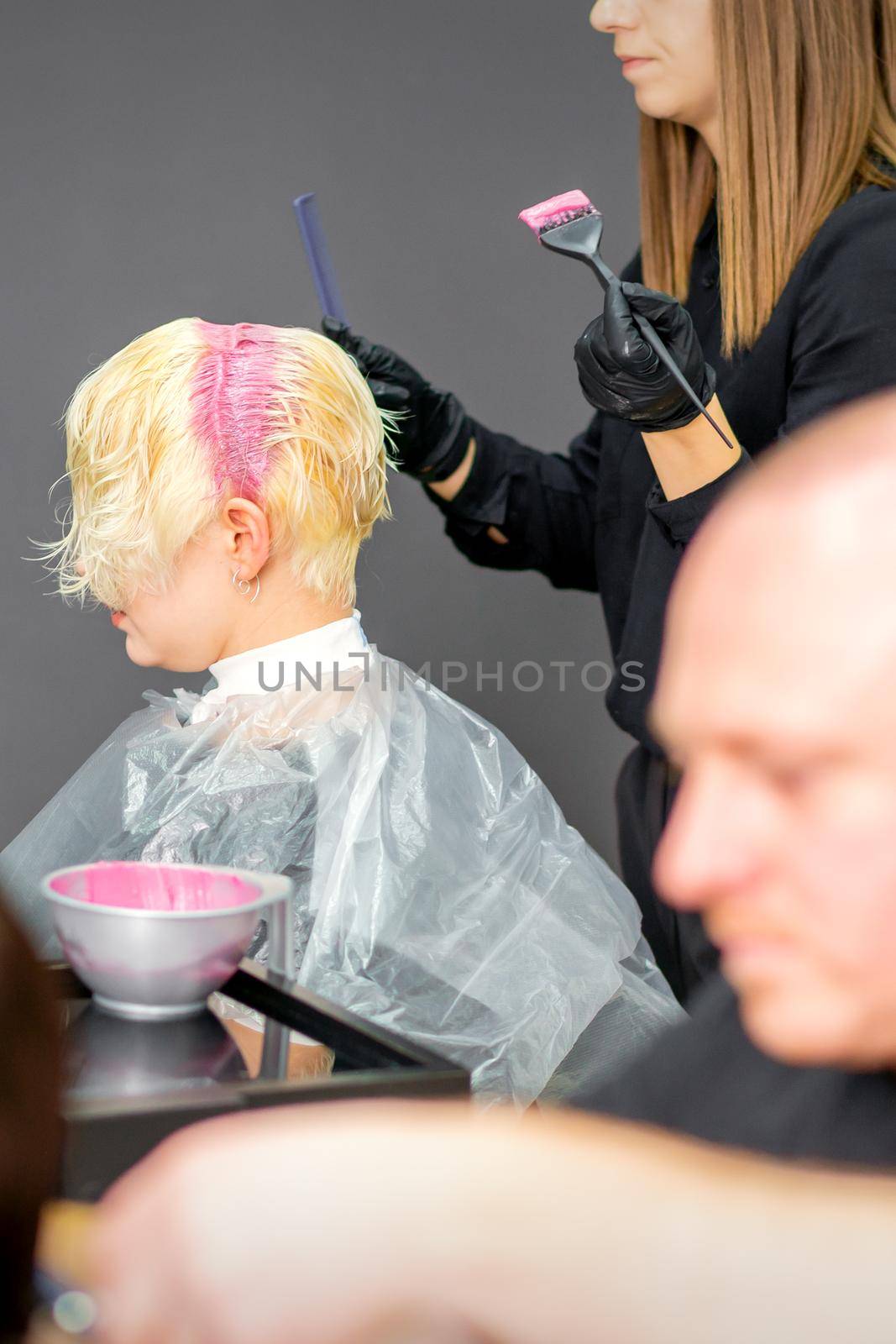 Coloring female hair in the hair salon. Young woman having her hair dyed by beautician at the beauty parlor. by okskukuruza