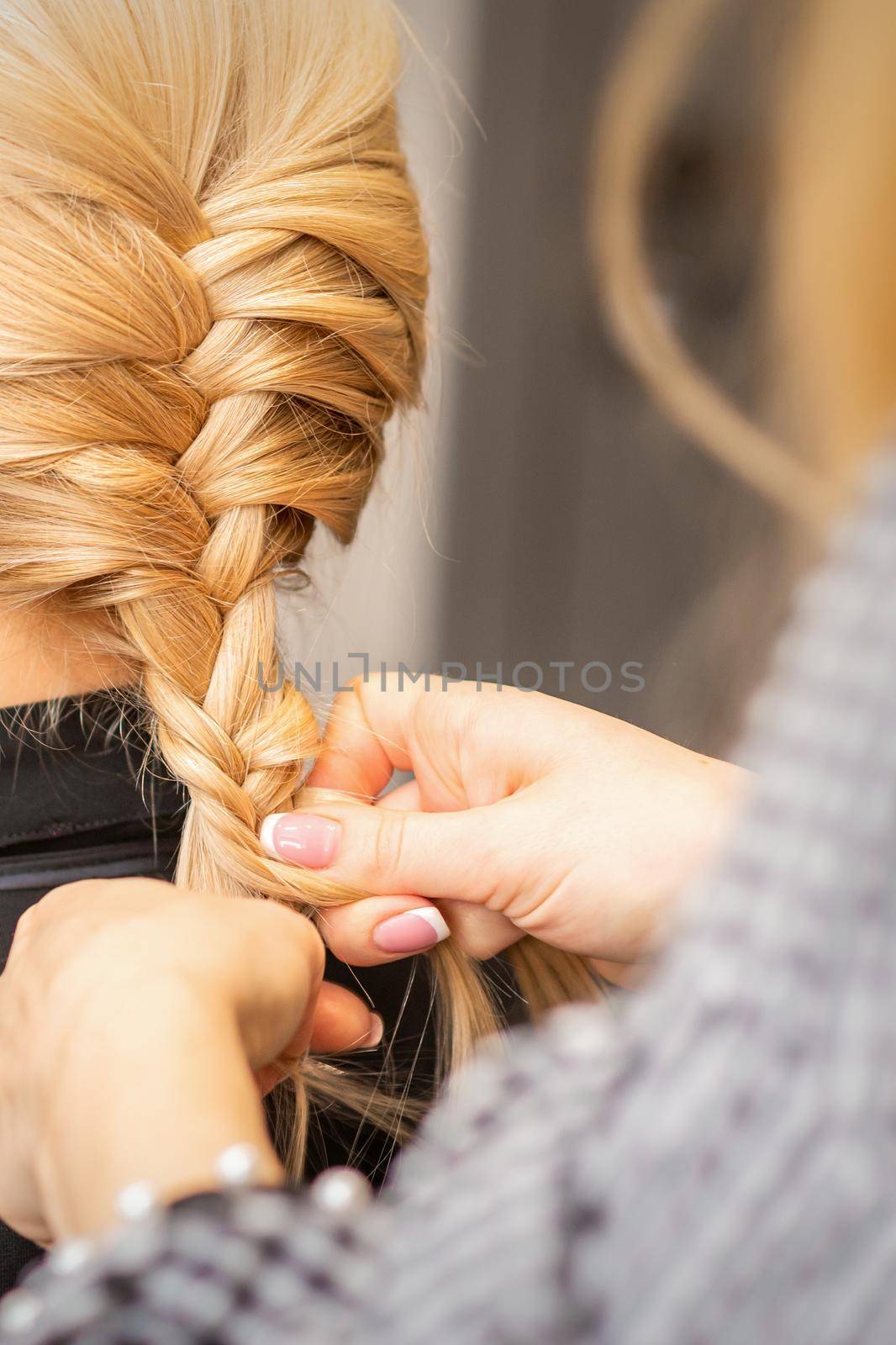 Braiding braid. Hands of female hairdresser braids long braid for a blonde woman in a hair salon. by okskukuruza