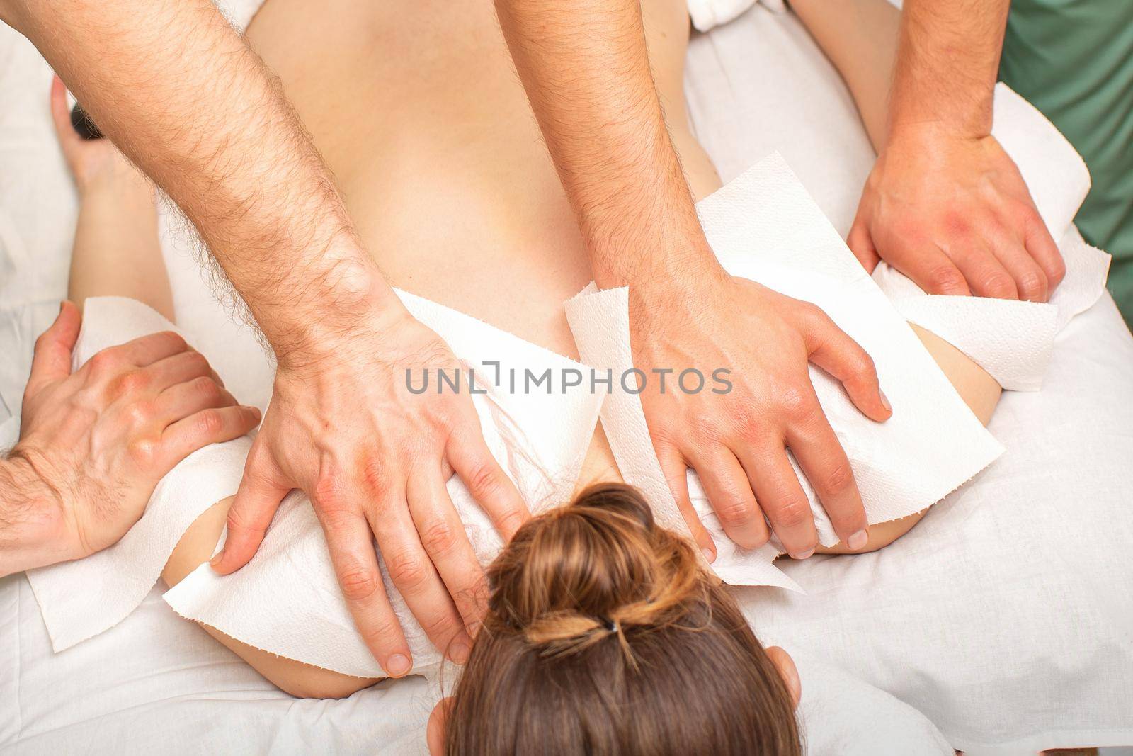 Back Massage with four hands in the spa salon. Two massage therapists make a back massage for a young woman